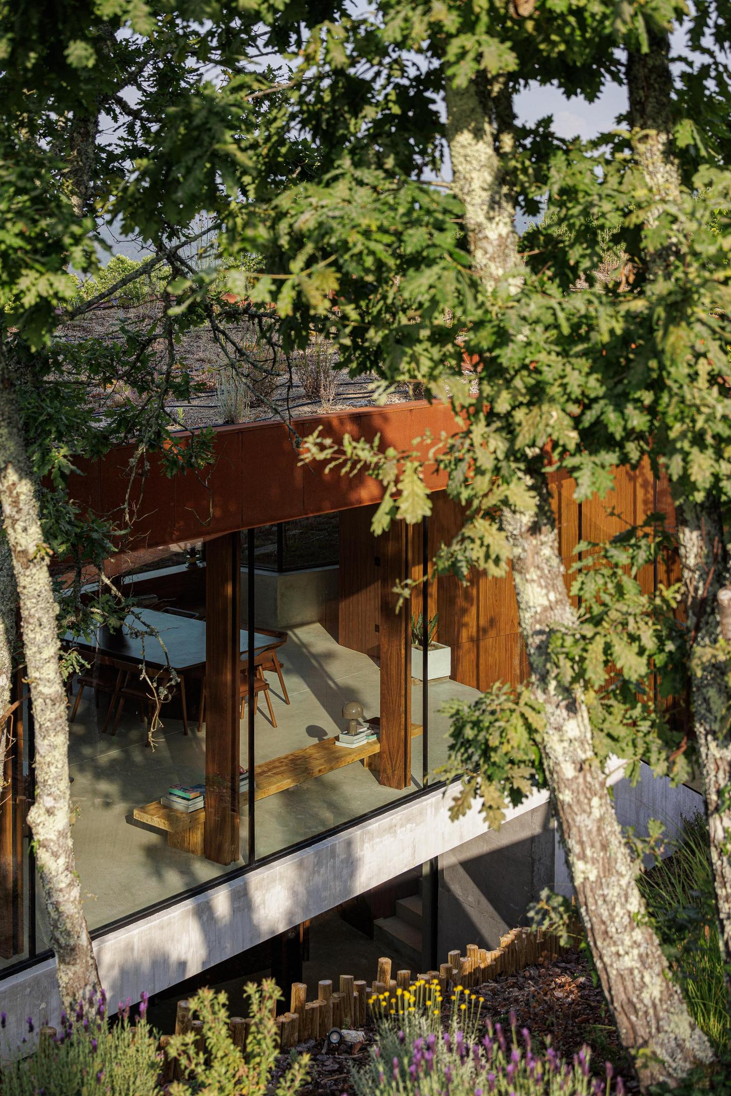 Sala de jantar: Interior com mesa de jantar em madeira, cadeiras de design e vista para o exterior. — Casa Corten arquitetura HPA Arquitetura e Investimentos em Celorico de Basto