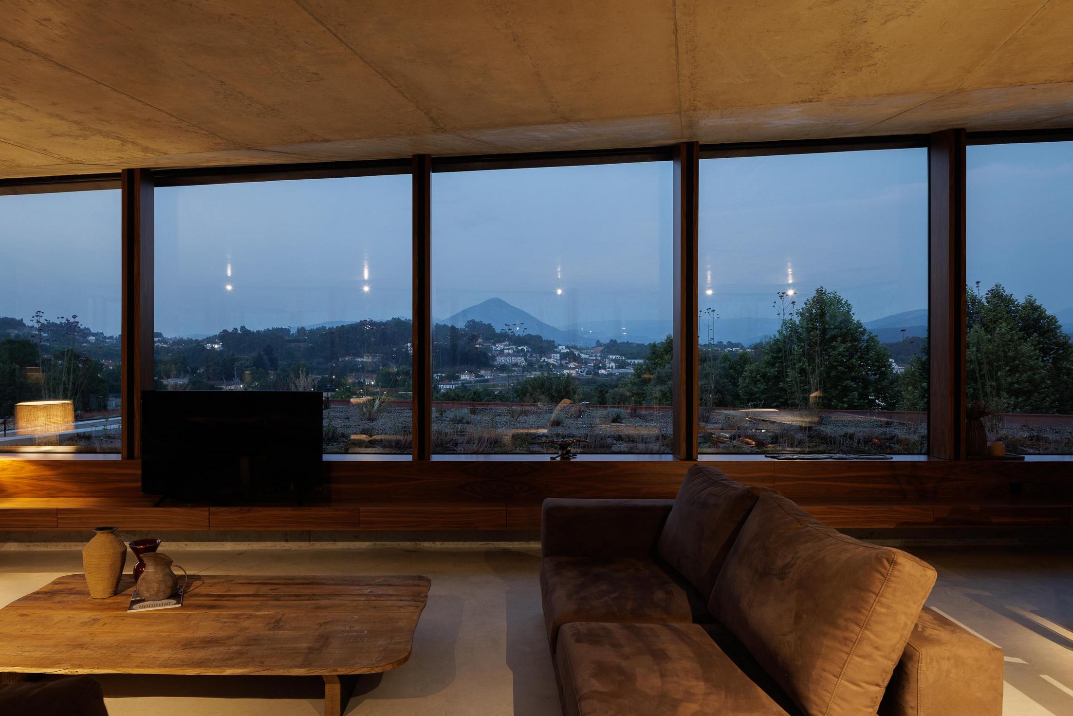 Exterior: Vista da casa iluminada ao anoitecer, com fachada envidraçada e telhado verde. — Casa Corten arquitetura HPA Arquitetura e Investimentos em Celorico de Basto
