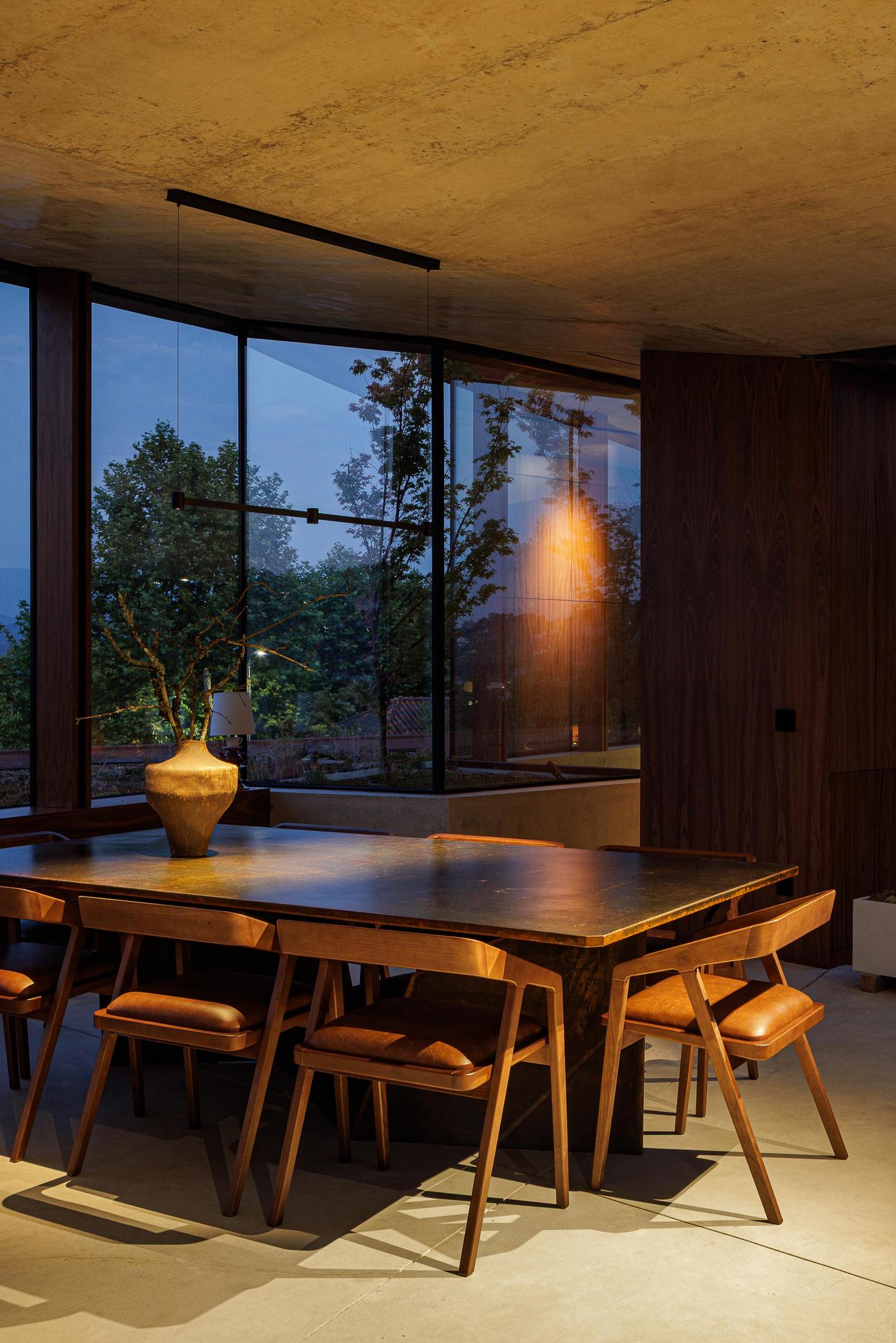 Exterior: Vista lateral da casa iluminada ao anoitecer, com fachada envidraçada e passadiço em aço corten. — Casa Corten arquitetura HPA Arquitetura e Investimentos em Celorico de Basto