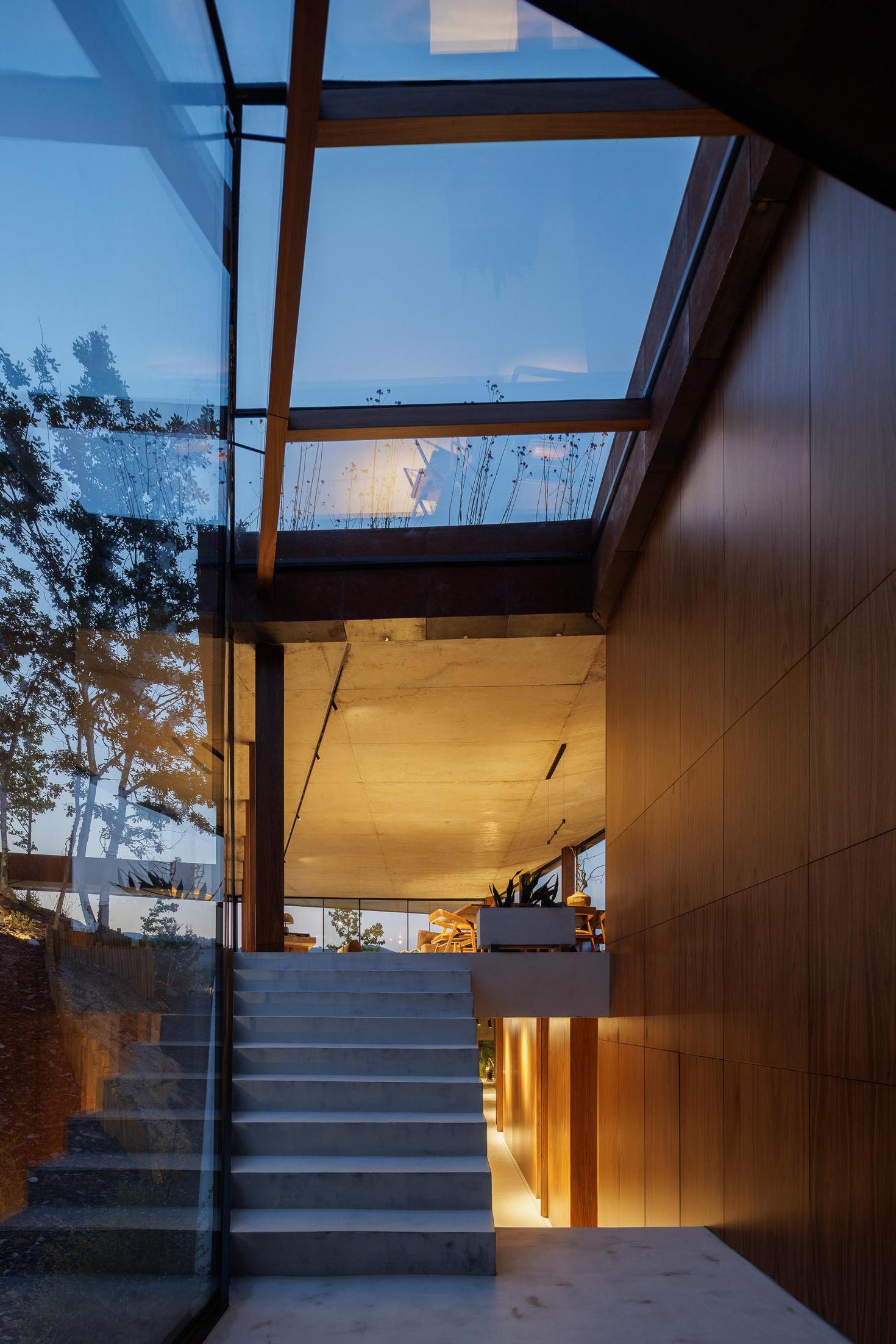 Exterior: Vista da casa iluminada ao anoitecer, com telhado verde e amplas janelas. — Casa Corten arquitetura HPA Arquitetura e Investimentos em Celorico de Basto