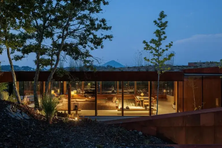 Quarto: Vista exterior do quarto iluminado ao anoitecer, com cama de casal e decora&ccedil;&atilde;o minimalista. &mdash; Casa Corten arquitetura HPA Arquitetura e Investimentos em Celorico de Basto