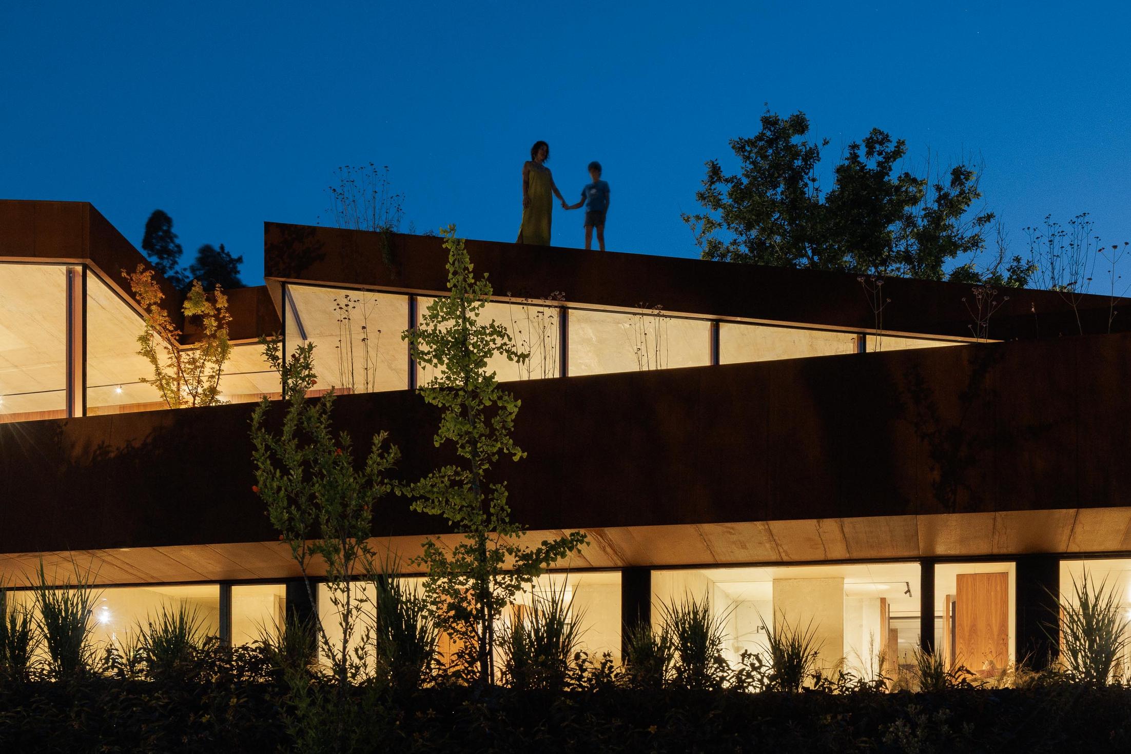 Exterior: Fachada da casa com revestimento em aço corten, grandes janelas e estrutura suspensa sobre pilares. — Casa Corten arquitetura HPA Arquitetura e Investimentos em Celorico de Basto