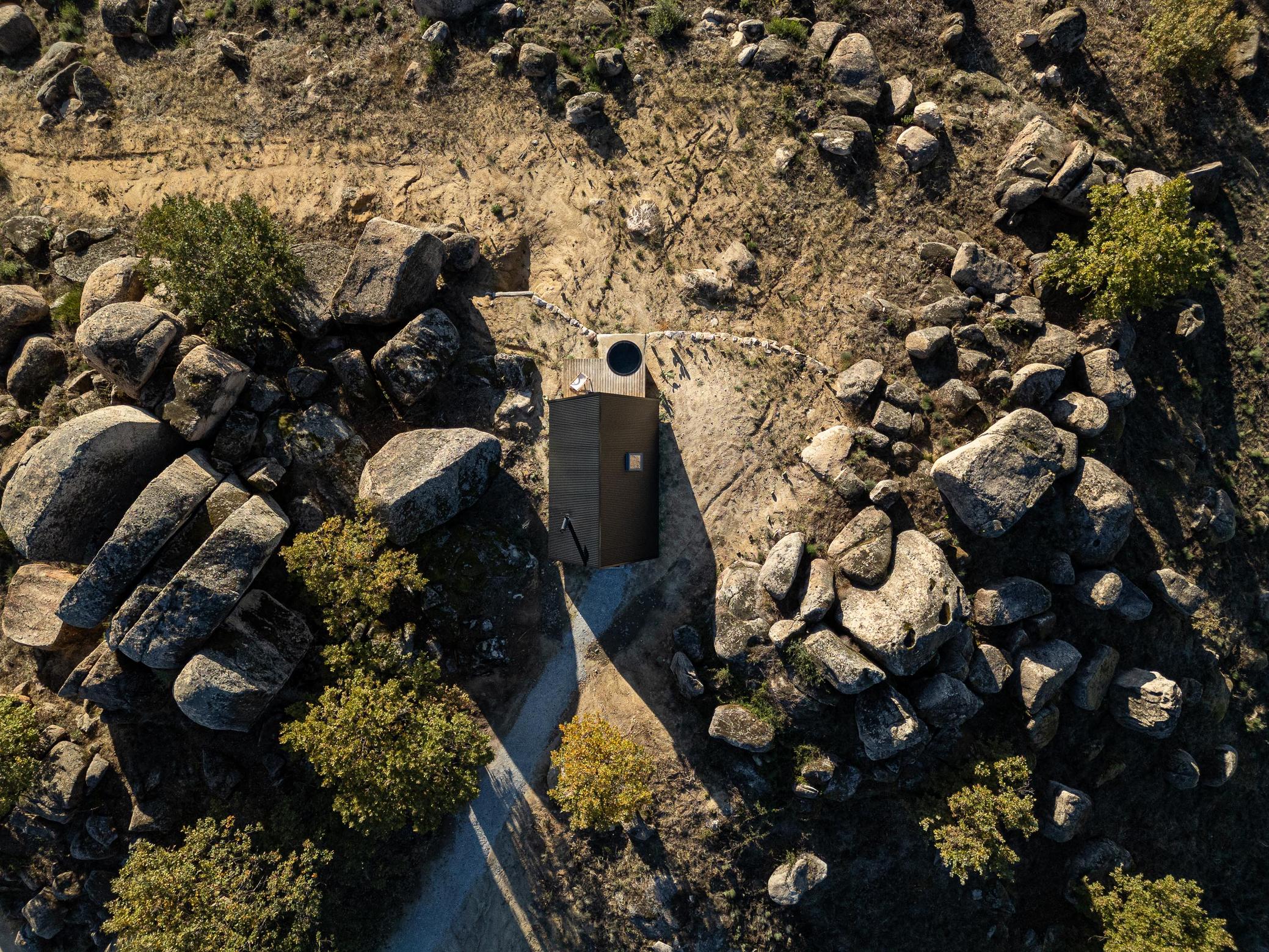 Vista aérea da cabana triangular inserida na paisagem rochosa e arborizada. — Abrigos de Montanha arquitetura Filipe Pina Arquitectura em Belmonte