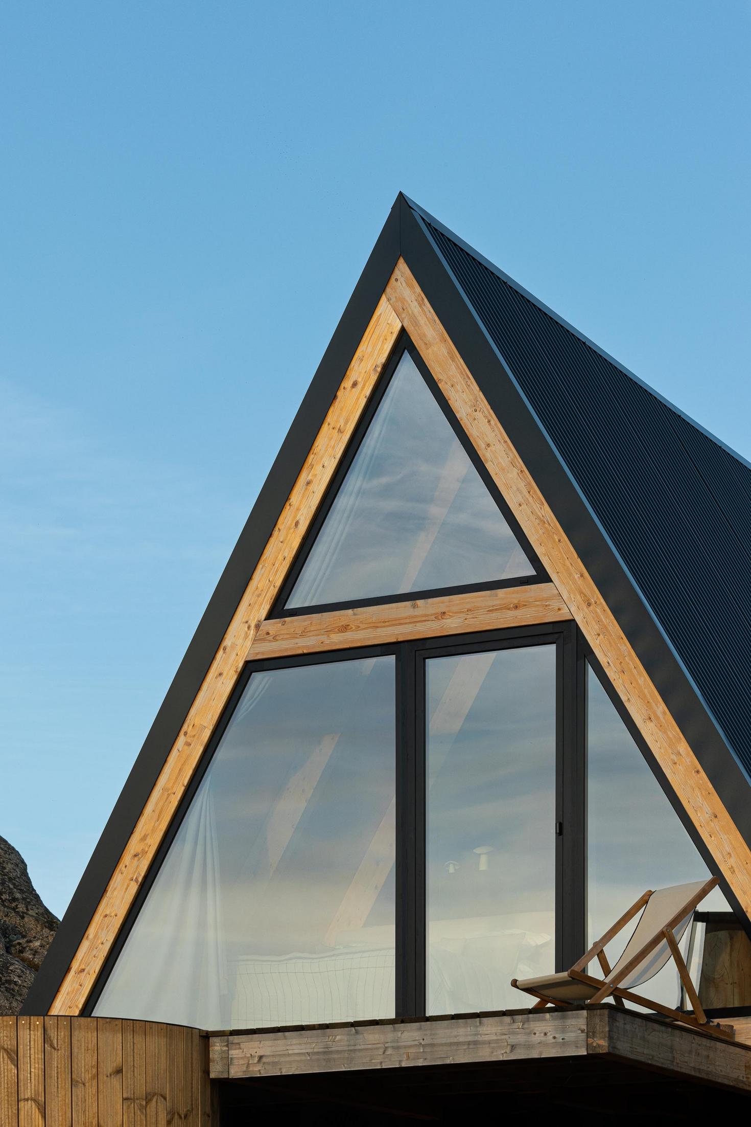 Exterior da cabana com estrutura triangular de madeira e porta de vidro. Espreguiçadeira no deck. — Abrigos de Montanha arquitetura Filipe Pina Arquitectura em Belmonte