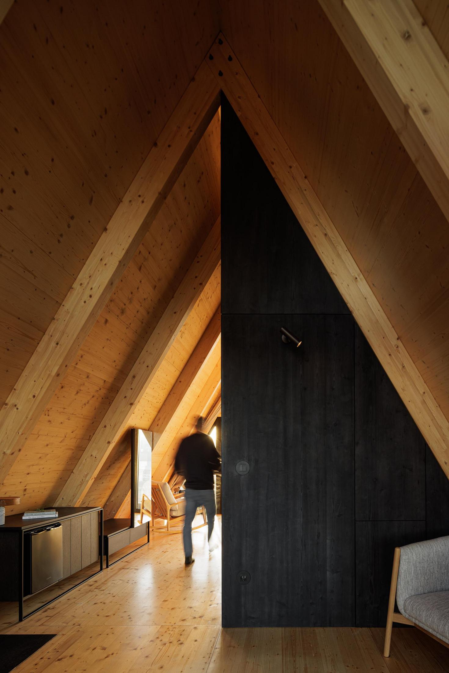 Interior com corredor de pavimento de madeira clara, paredes e teto revestidos a madeira. Porta escura. — Abrigos de Montanha arquitetura Filipe Pina Arquitectura em Belmonte