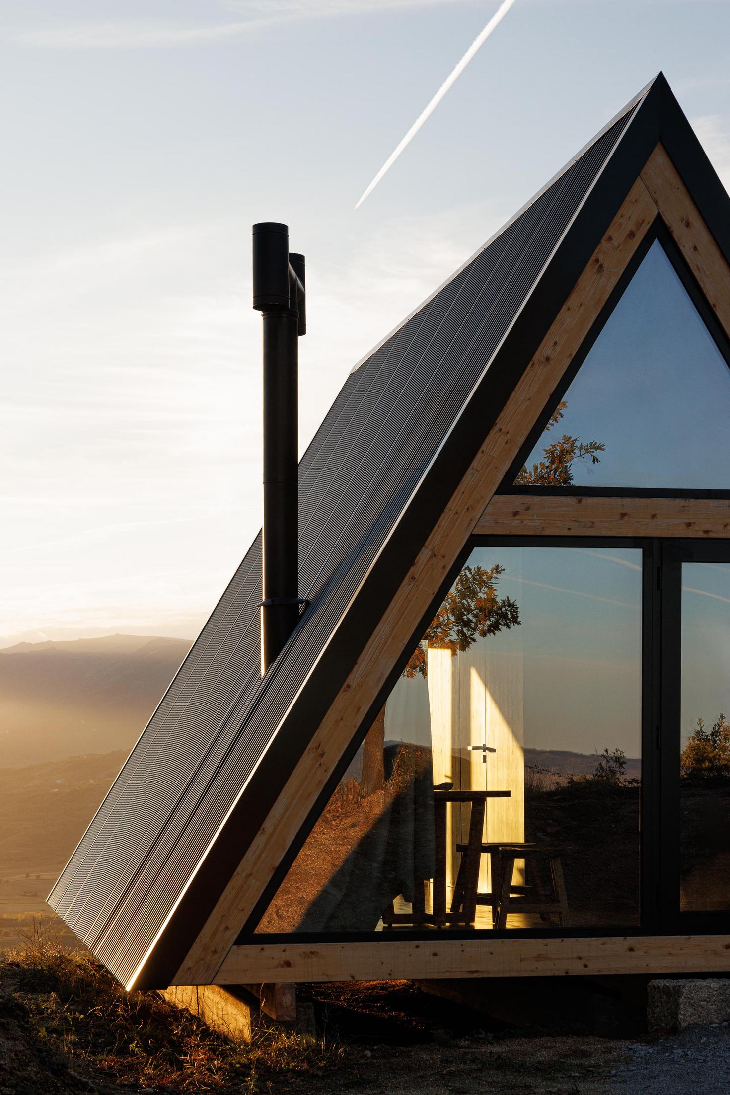 Exterior da cabana triangular com revestimento metálico e estrutura de madeira. Paisagem montanhosa ao fundo. — Abrigos de Montanha arquitetura Filipe Pina Arquitectura em Belmonte