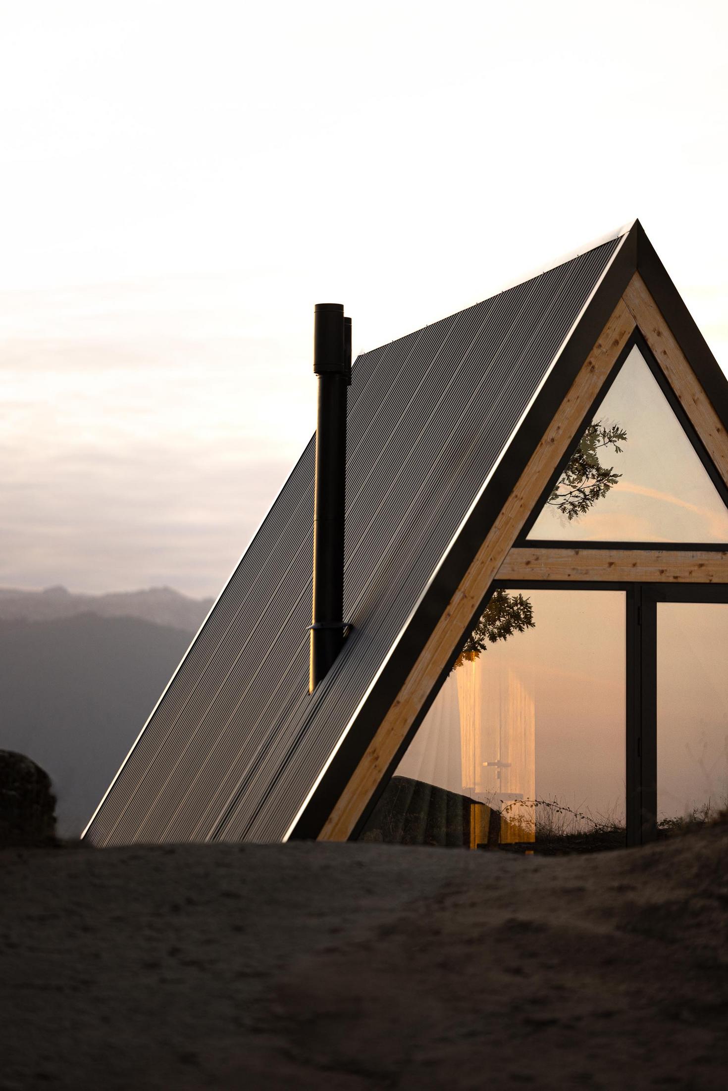 Exterior da cabana triangular com revestimento metálico e estrutura de madeira. Paisagem montanhosa ao fundo. — Abrigos de Montanha arquitetura Filipe Pina Arquitectura em Belmonte