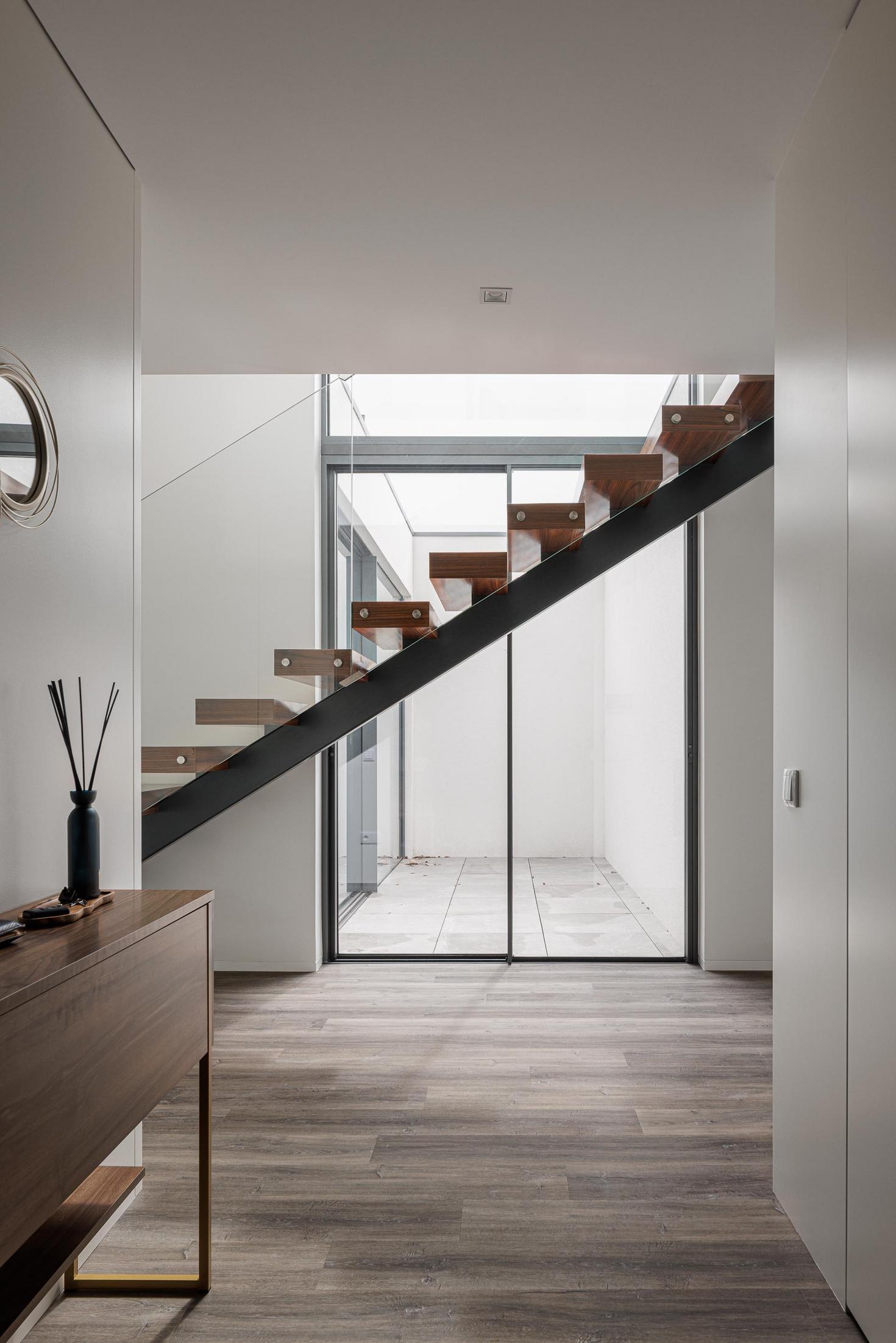 Hall de entrada: Escada flutuante em madeira e aço, com luz natural e consola de madeira. — Casa dos Sobreiros II arquitetura Urbanpolis em Póvoa de Varzim