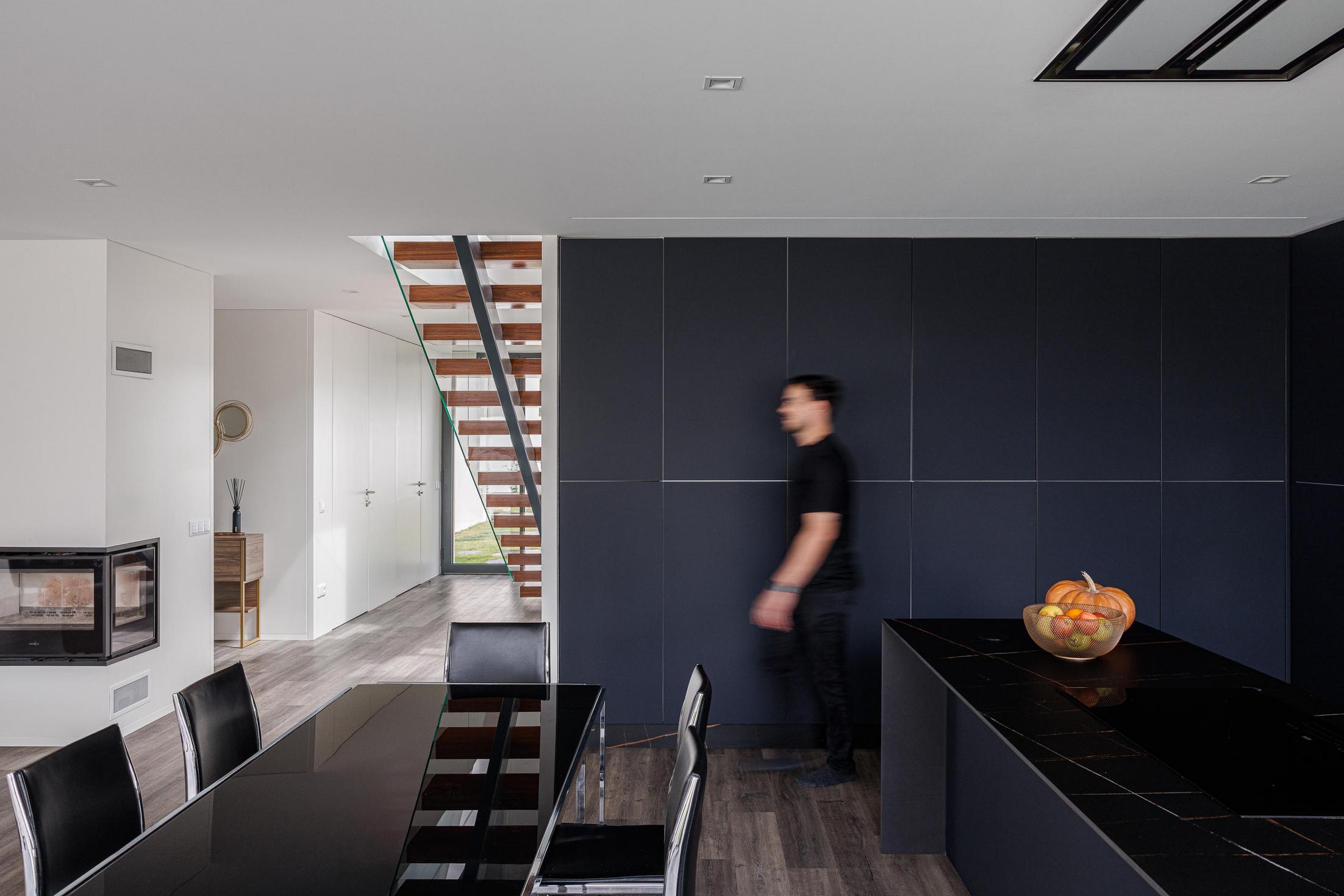 Sala de jantar/Cozinha: Mesa de jantar preta, cozinha preta minimalista e escada flutuante. — Casa dos Sobreiros II arquitetura Urbanpolis em Póvoa de Varzim