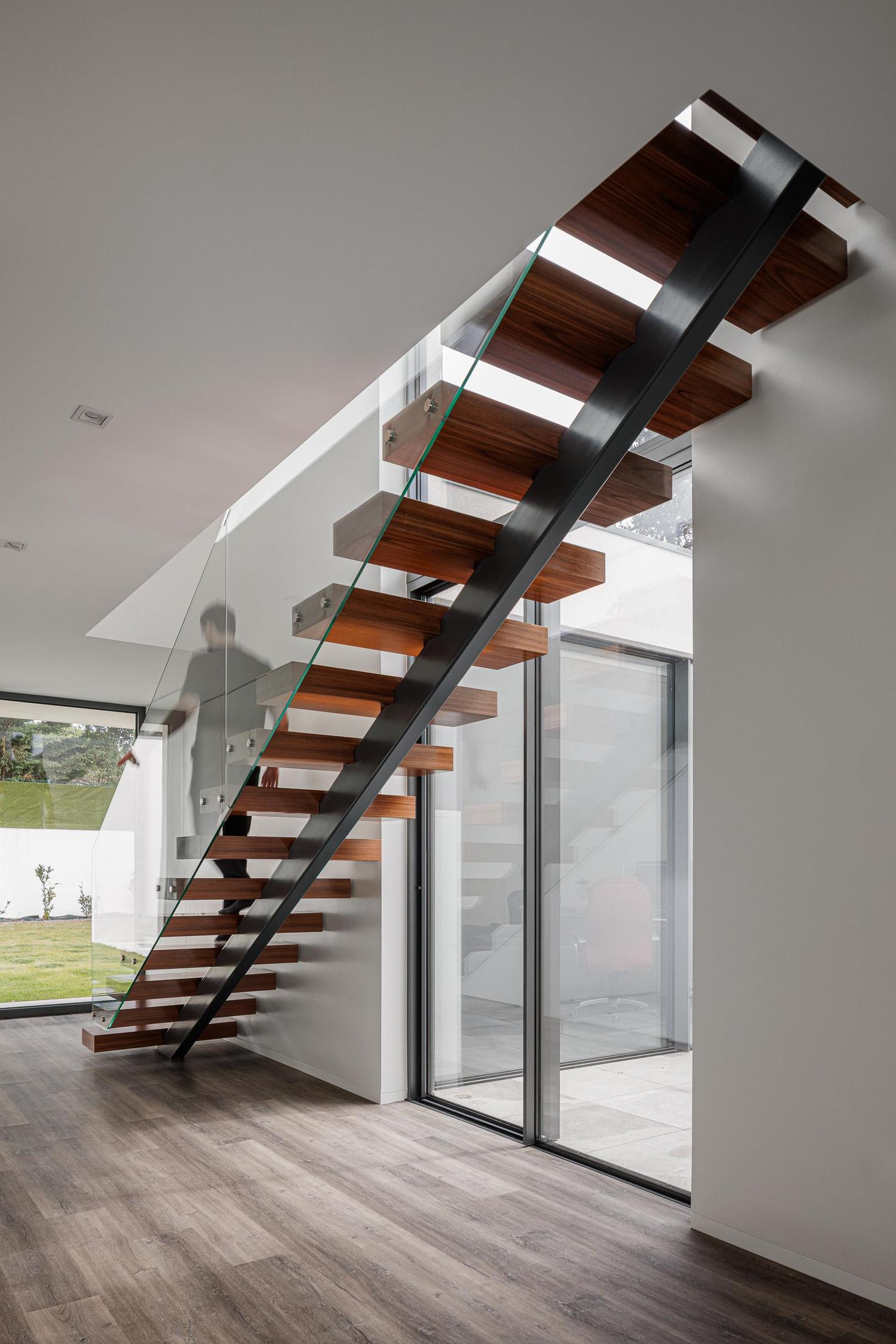 Escada: Detalhe da escada flutuante em madeira e aço com guarda em vidro. — Casa dos Sobreiros II arquitetura Urbanpolis em Póvoa de Varzim