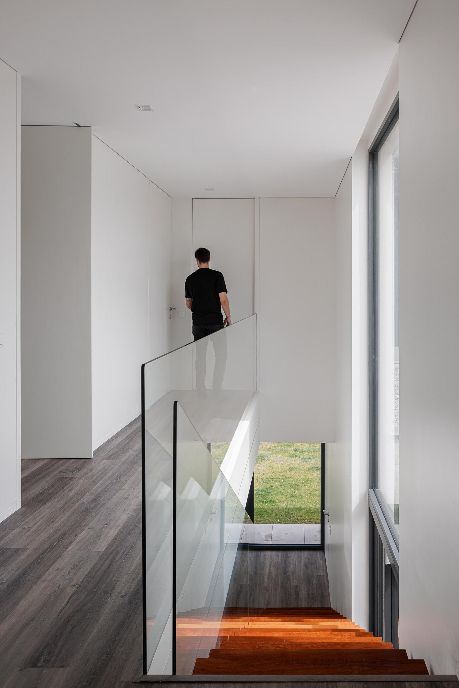 Corredor: Corredor branco com escada flutuante e vista para o exterior. — Casa dos Sobreiros II arquitetura Urbanpolis em Póvoa de Varzim