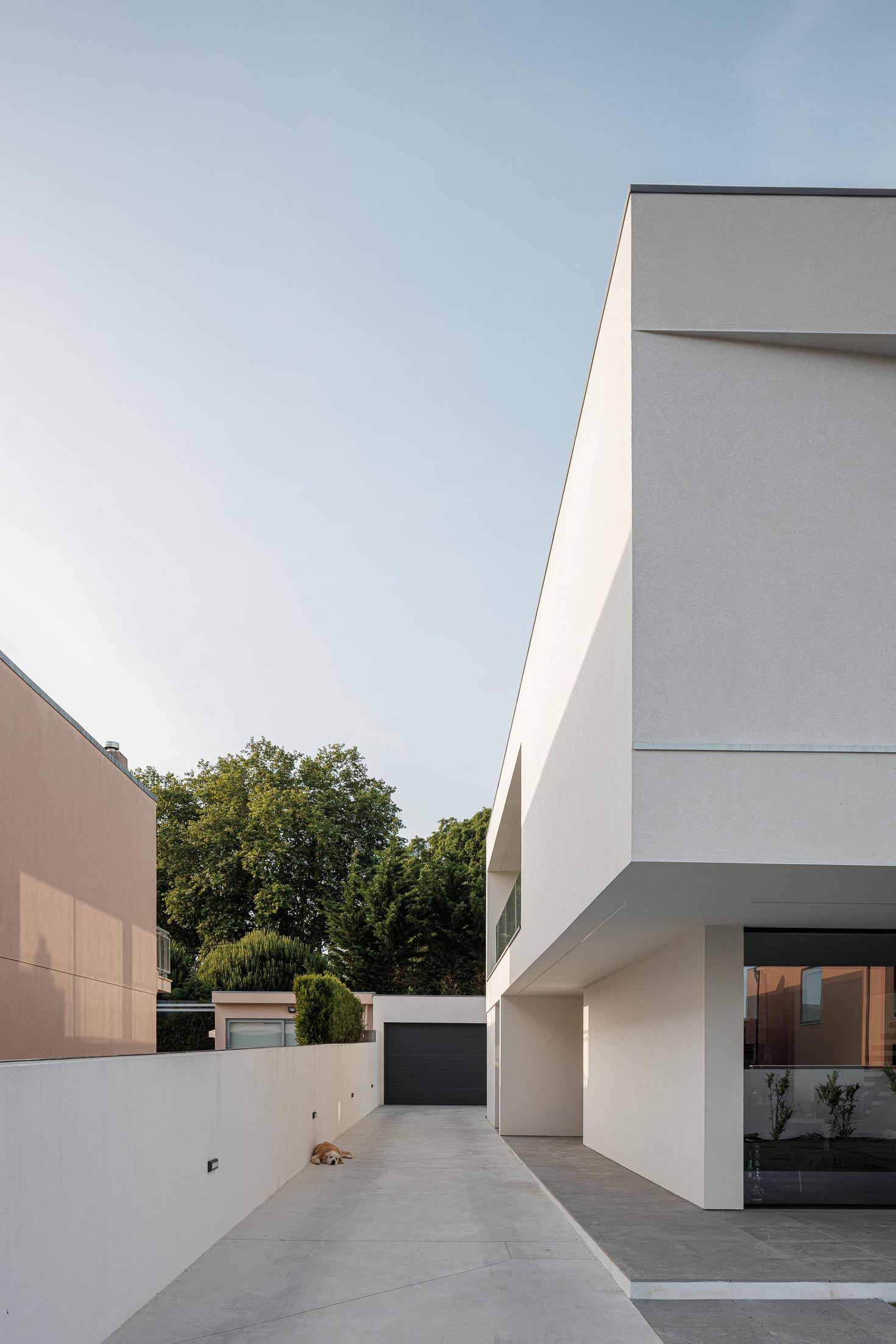 Exterior: Moradia branca com garagem e cão deitado na entrada. — Casa dos Sobreiros II arquitetura Urbanpolis em Póvoa de Varzim