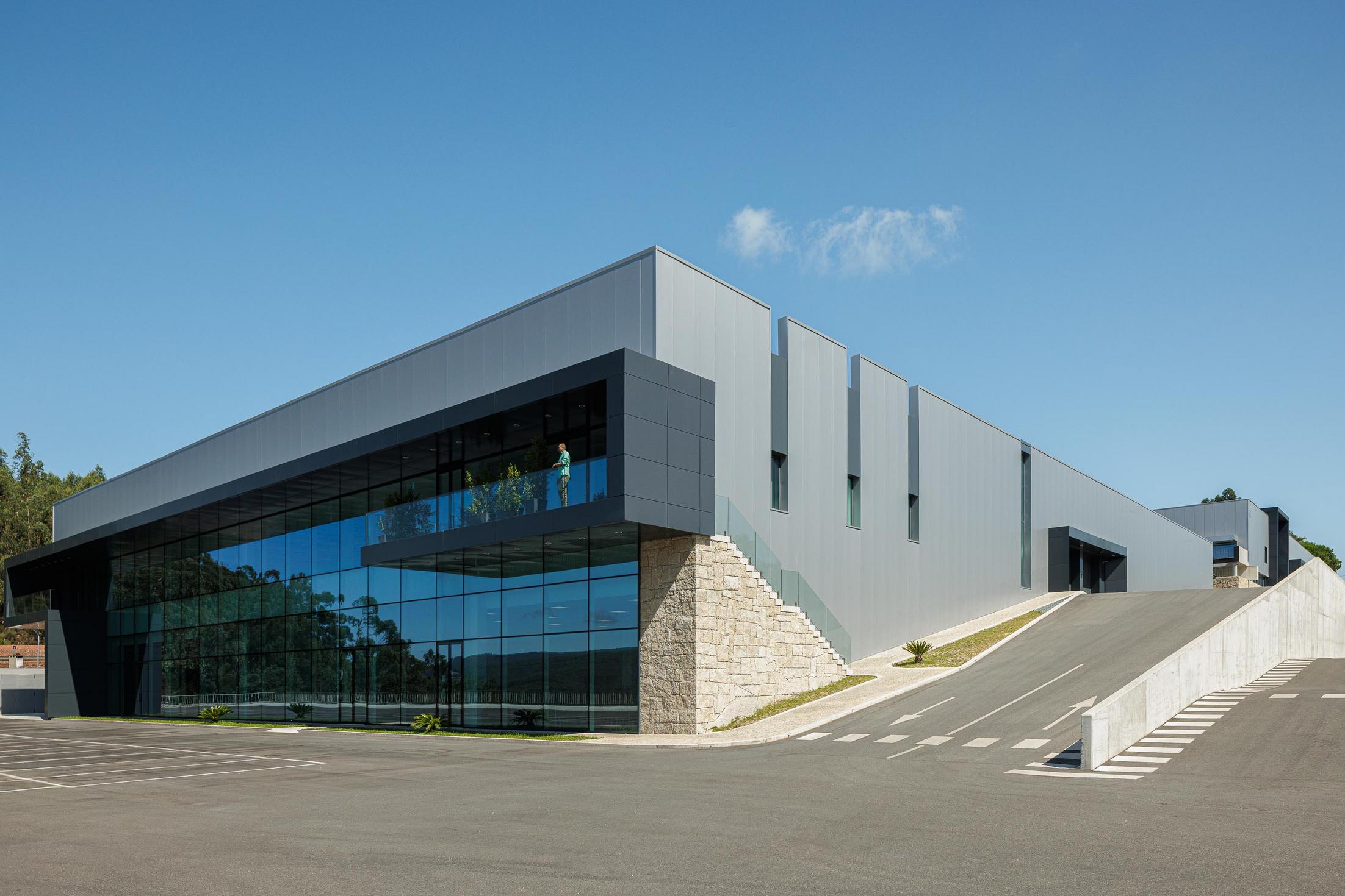 Fachada principal: Edifício industrial com fachada envidraçada e volume saliente com varanda. — Bradco II arquitetura Em Paralelo em Castelo de Paiva