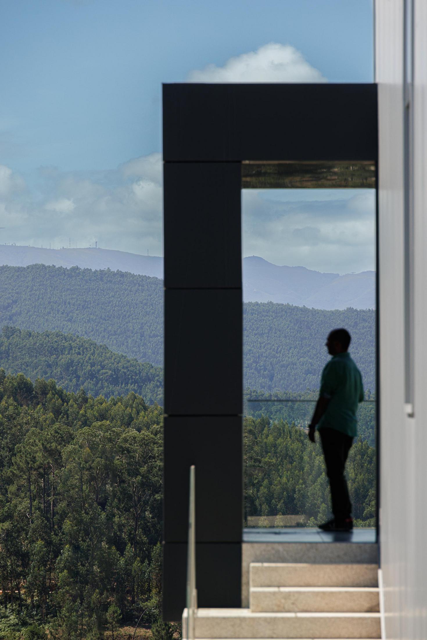Varanda: Pessoa a observar a paisagem através da abertura do volume saliente. — Bradco II arquitetura Em Paralelo em Castelo de Paiva