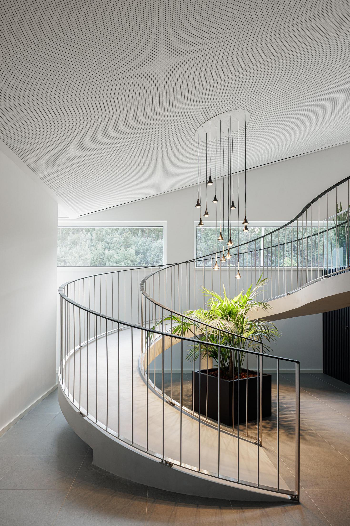 Escadaria interior: Detalhe da escada em caracol com candeeiro e plantas. — Bradco II arquitetura Em Paralelo em Castelo de Paiva