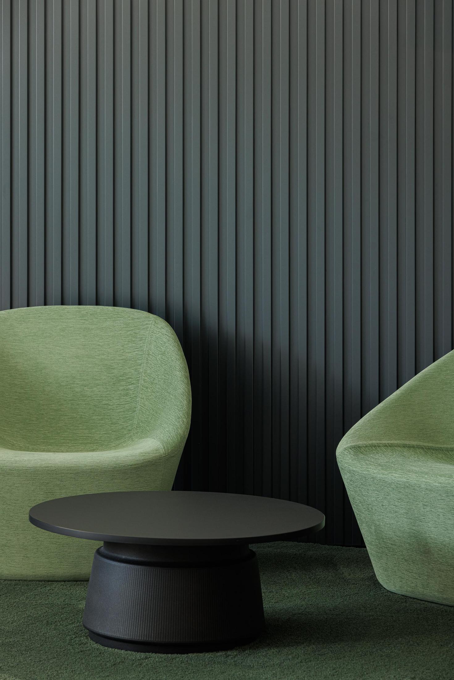 Sala de espera: Cadeiras verdes, mesa preta e parede com revestimento vertical. — Bradco II arquitetura Em Paralelo em Castelo de Paiva
