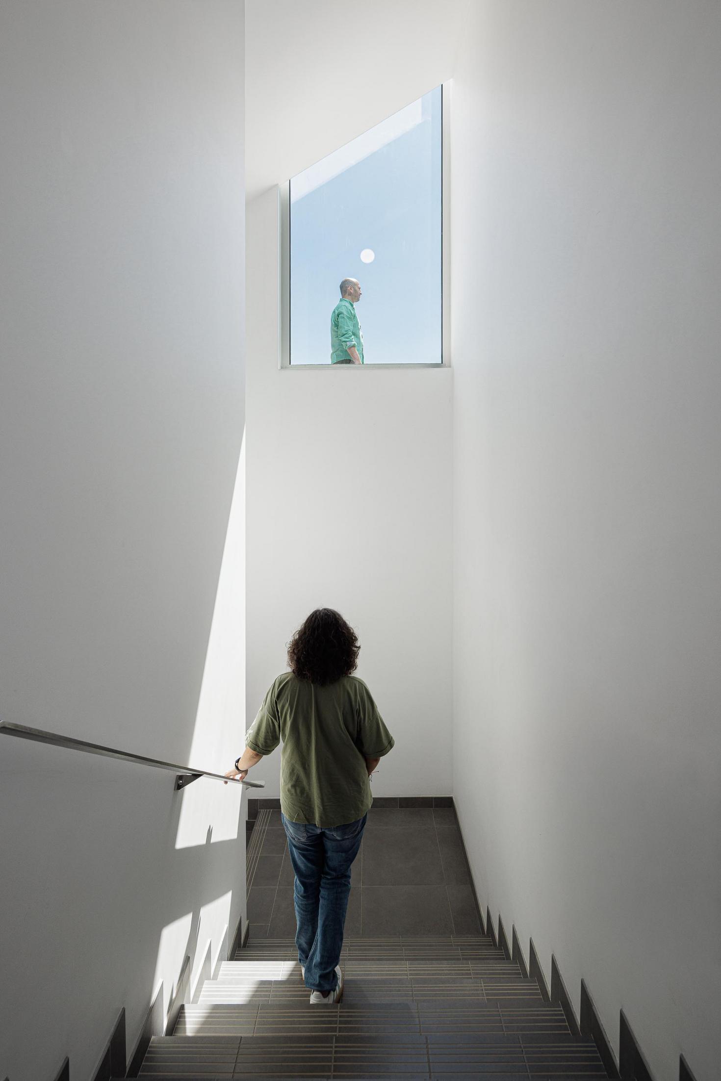 Escadaria interior: Escada com corrimão metálico e janela triangular no topo. — Bradco II arquitetura Em Paralelo em Castelo de Paiva