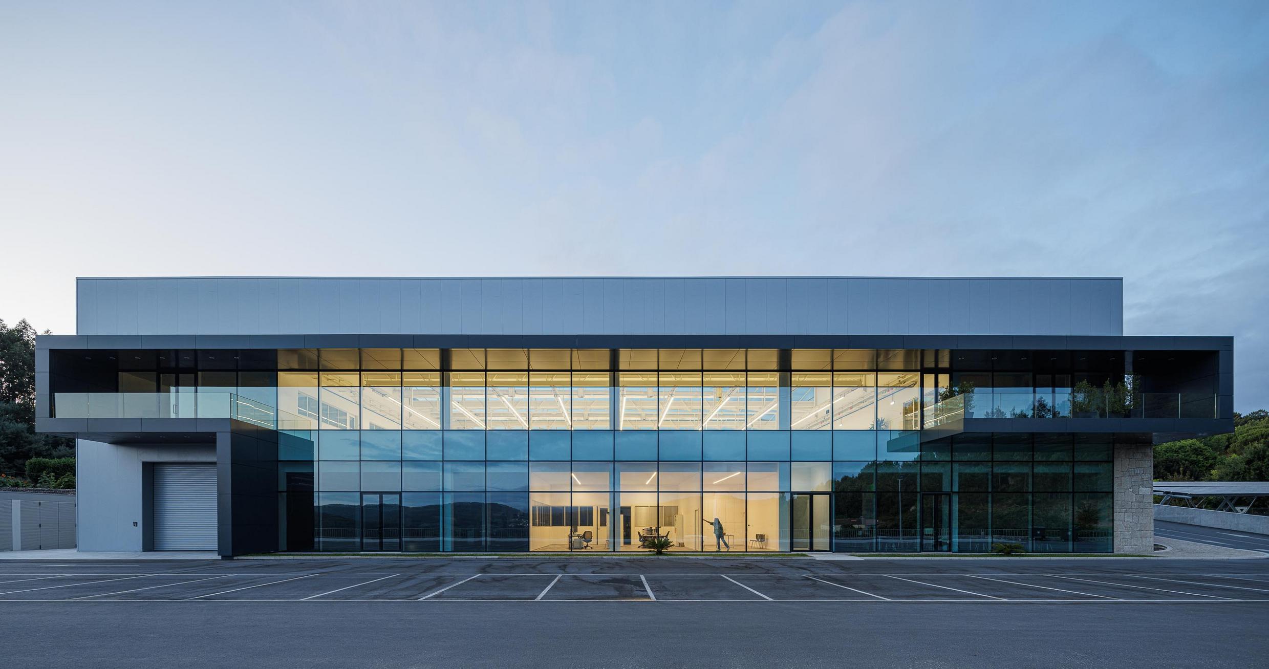 Fachada lateral: Edifício industrial com fachada envidraçada e porta de garagem. — Bradco II arquitetura Em Paralelo em Castelo de Paiva