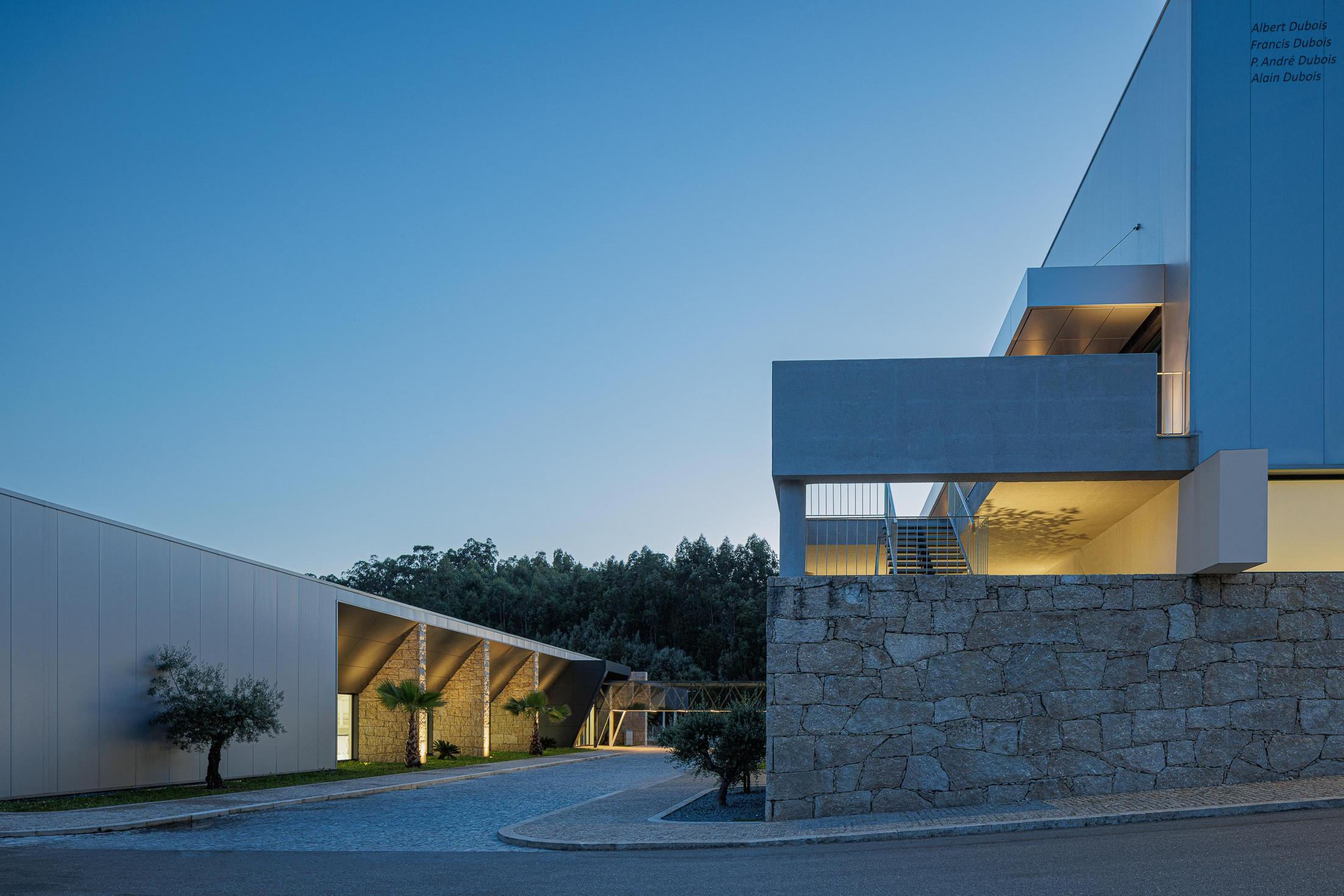 Cobertura: Vista noturna da cobertura com claraboias triangulares iluminadas. — Bradco II arquitetura Em Paralelo em Castelo de Paiva