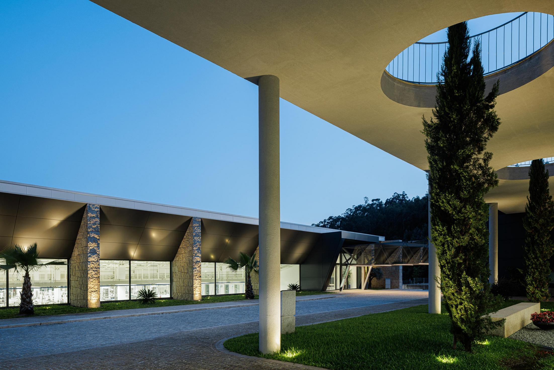Fachada principal: Vista noturna da fachada envidraçada com iluminação interior. — Bradco II arquitetura Em Paralelo em Castelo de Paiva