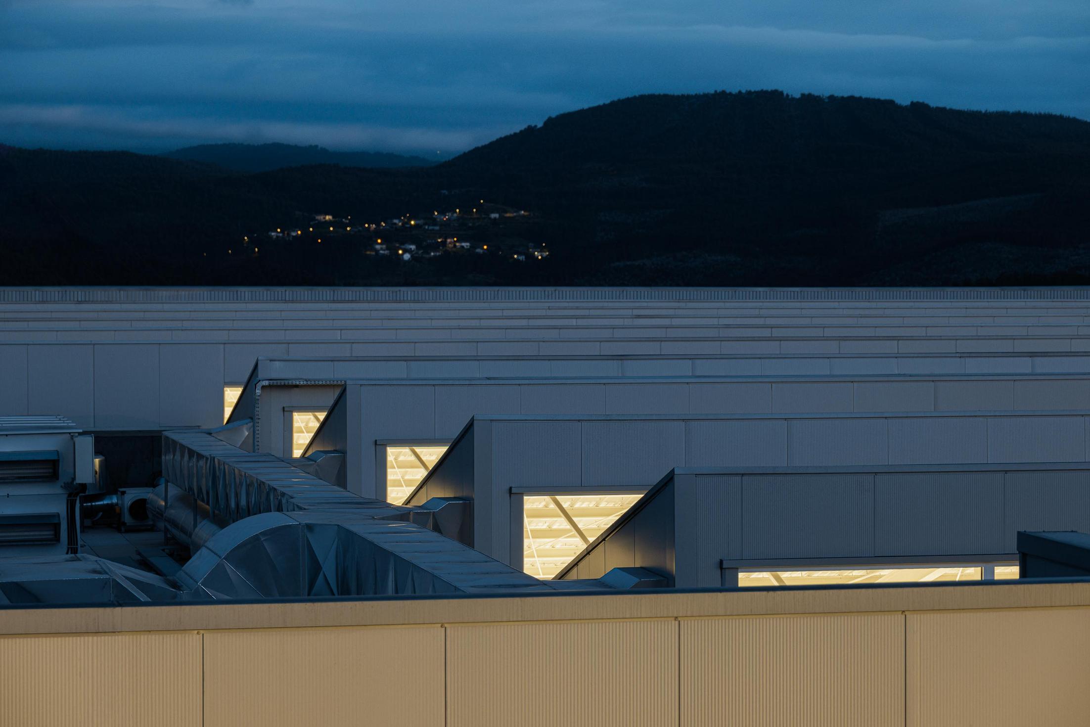 Fábrica: Vista noturna do interior da fábrica com iluminação industrial. — Bradco II arquitetura Em Paralelo em Castelo de Paiva