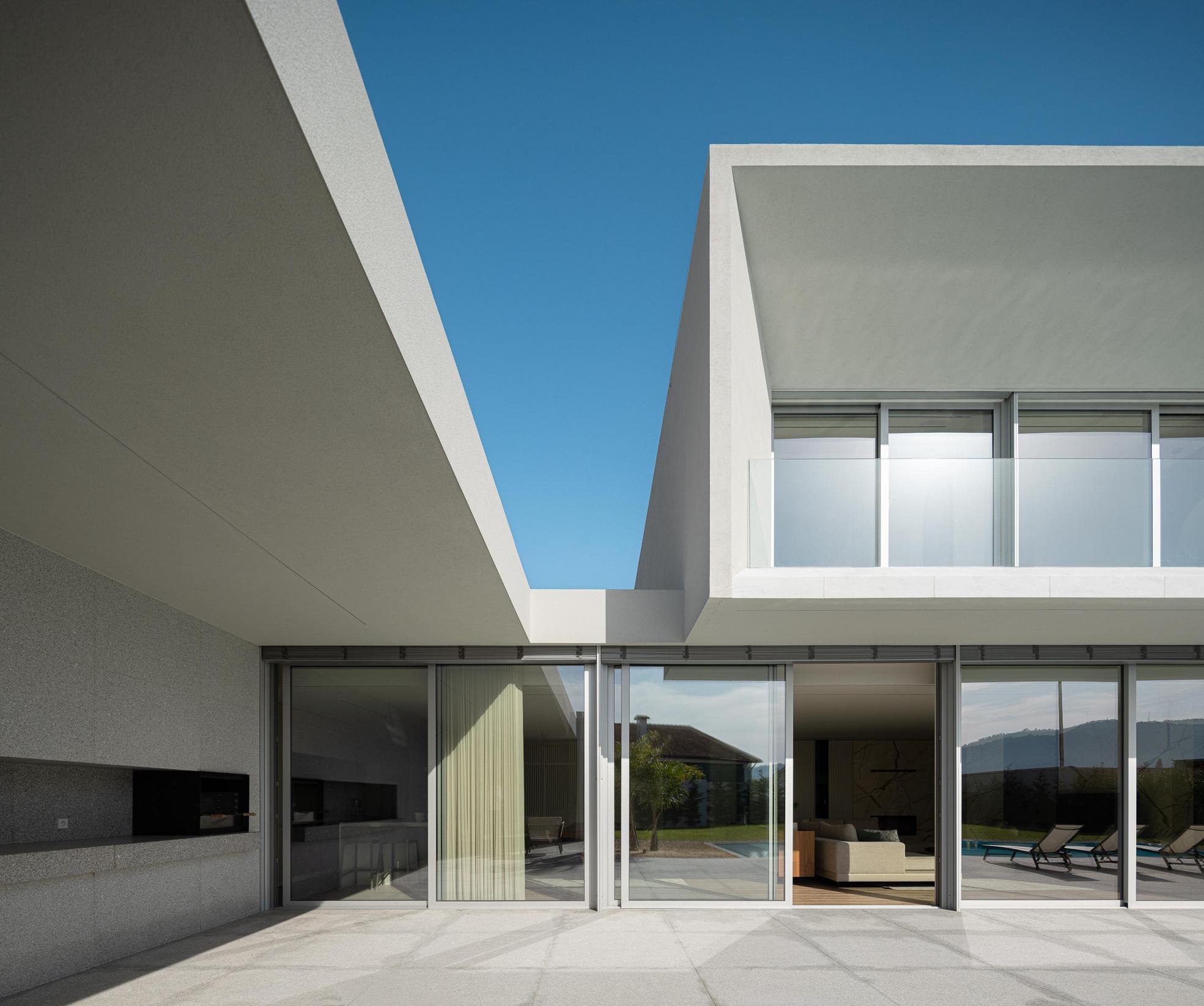 Exterior: Detalhe da fachada posterior com grandes janelas e alpendre com zona de refeições. — Casa Branca Minimalista arquitetura Arquitetura501 em Braga