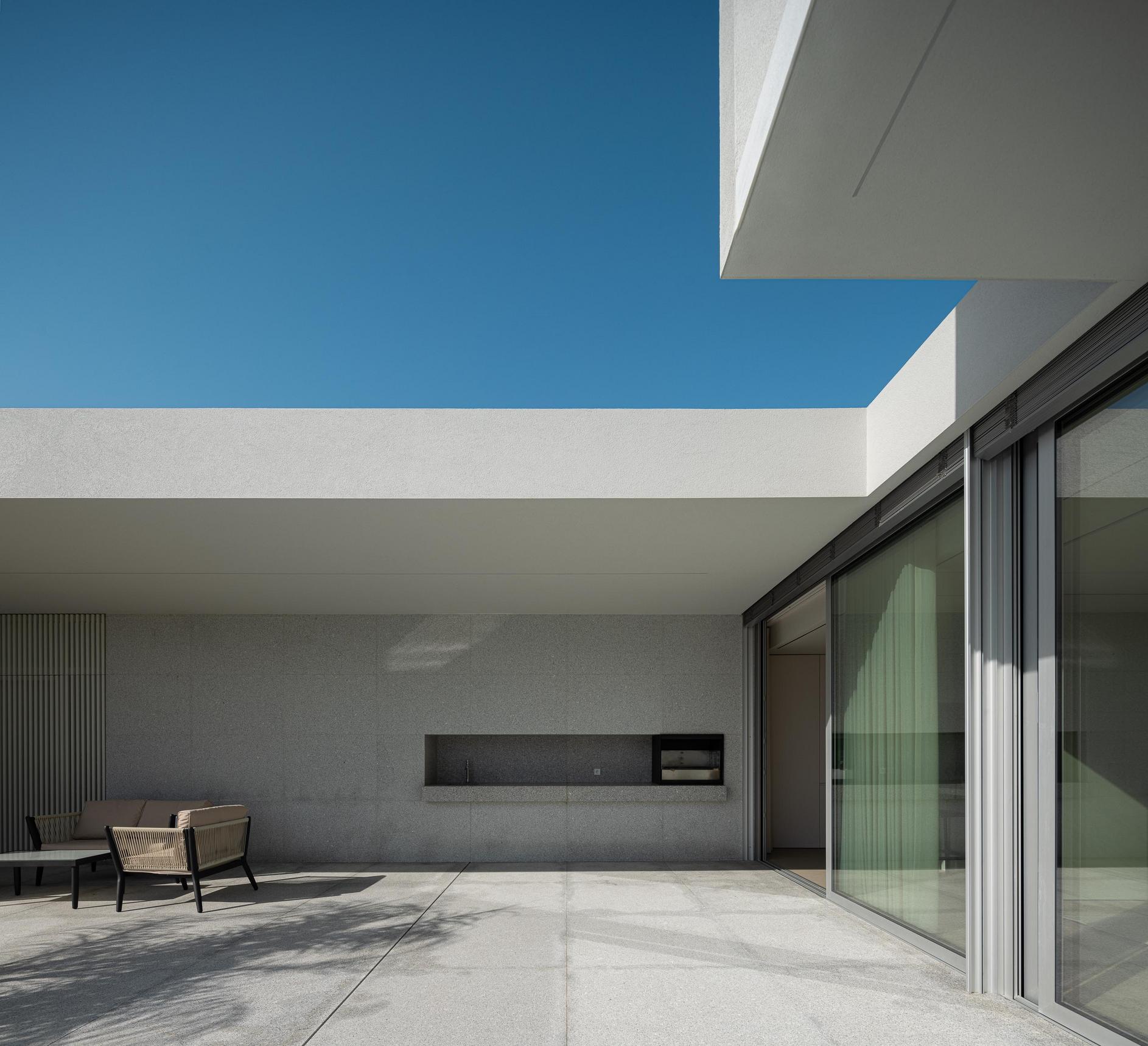 Exterior: Alpendre com zona de estar e churrasqueira, pavimento em pedra. — Casa Branca Minimalista arquitetura Arquitetura501 em Braga