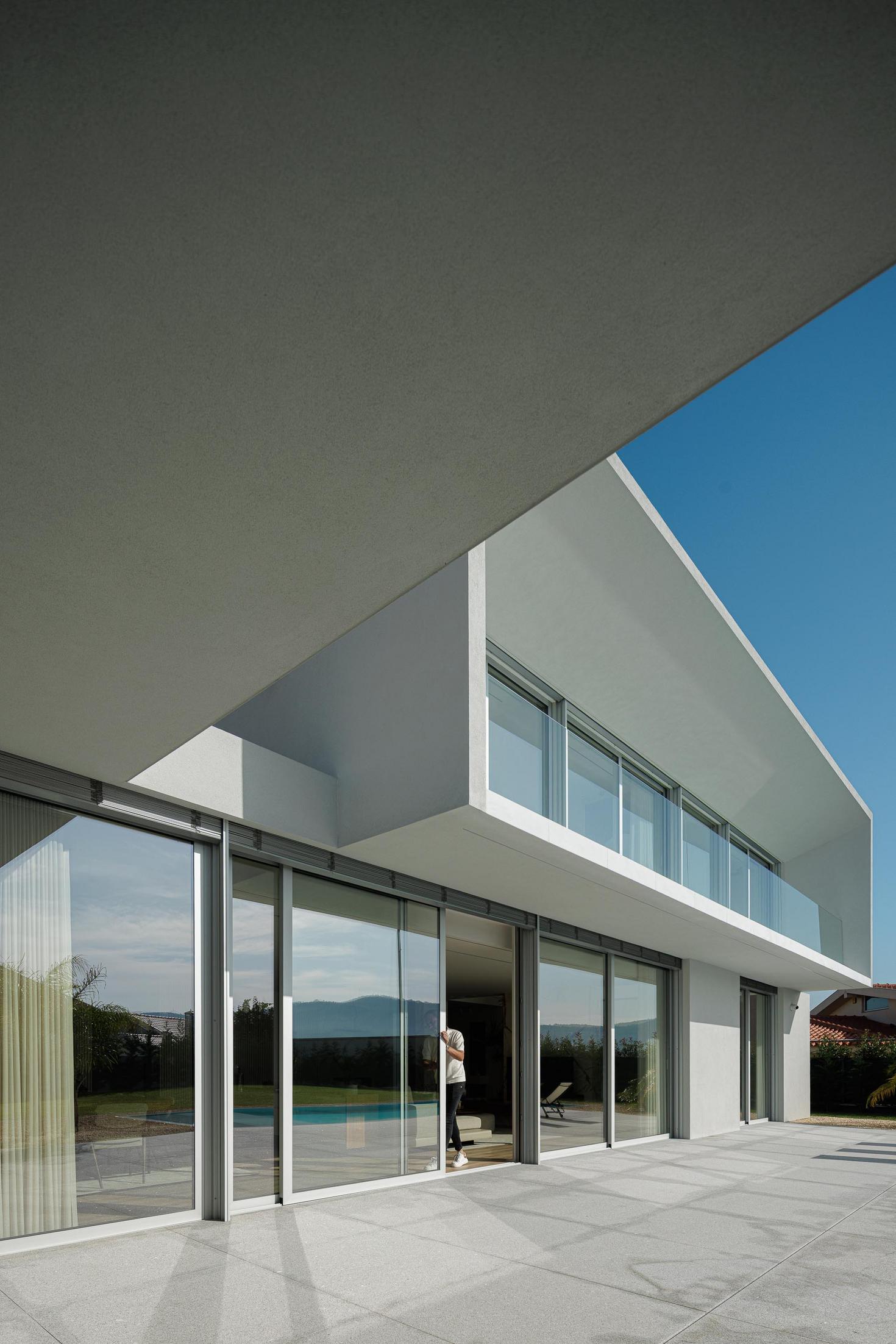 Exterior: Fachada posterior da casa com grandes janelas e varanda no piso superior. — Casa Branca Minimalista arquitetura Arquitetura501 em Braga