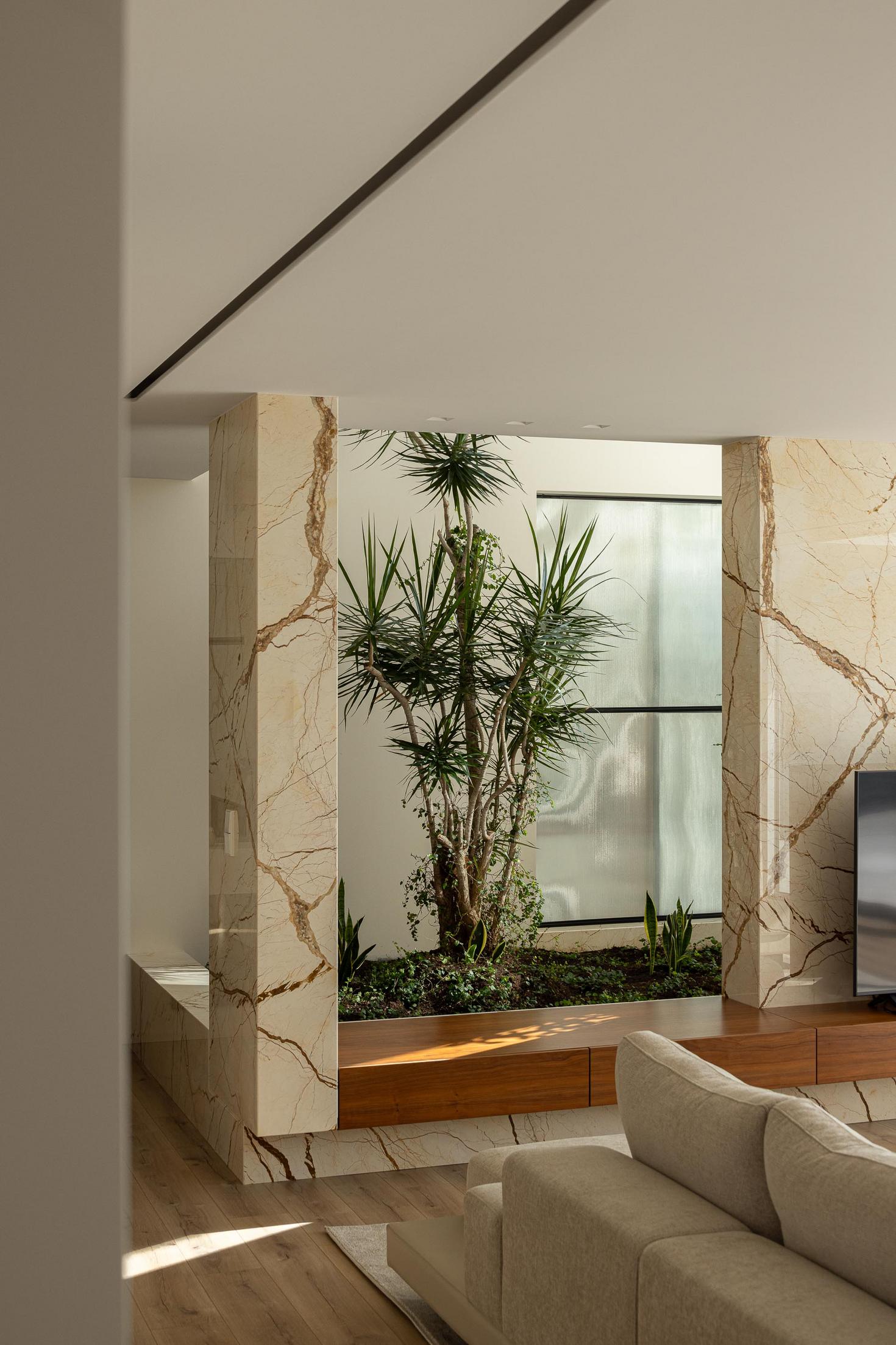 Jardim interior: Vegetação exuberante sob claraboia, com paredes revestidas a mármore. — Casa Branca Minimalista arquitetura Arquitetura501 em Braga