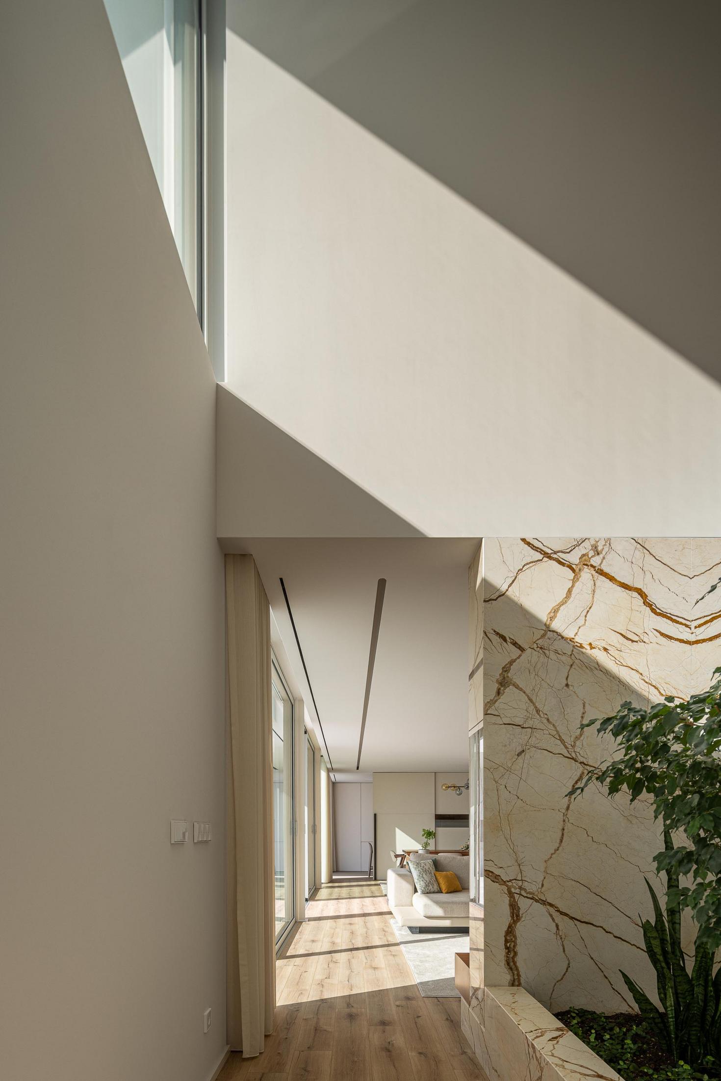 Corredor: Vista para a sala de estar através do jardim interior, com paredes em mármore. — Casa Branca Minimalista arquitetura Arquitetura501 em Braga