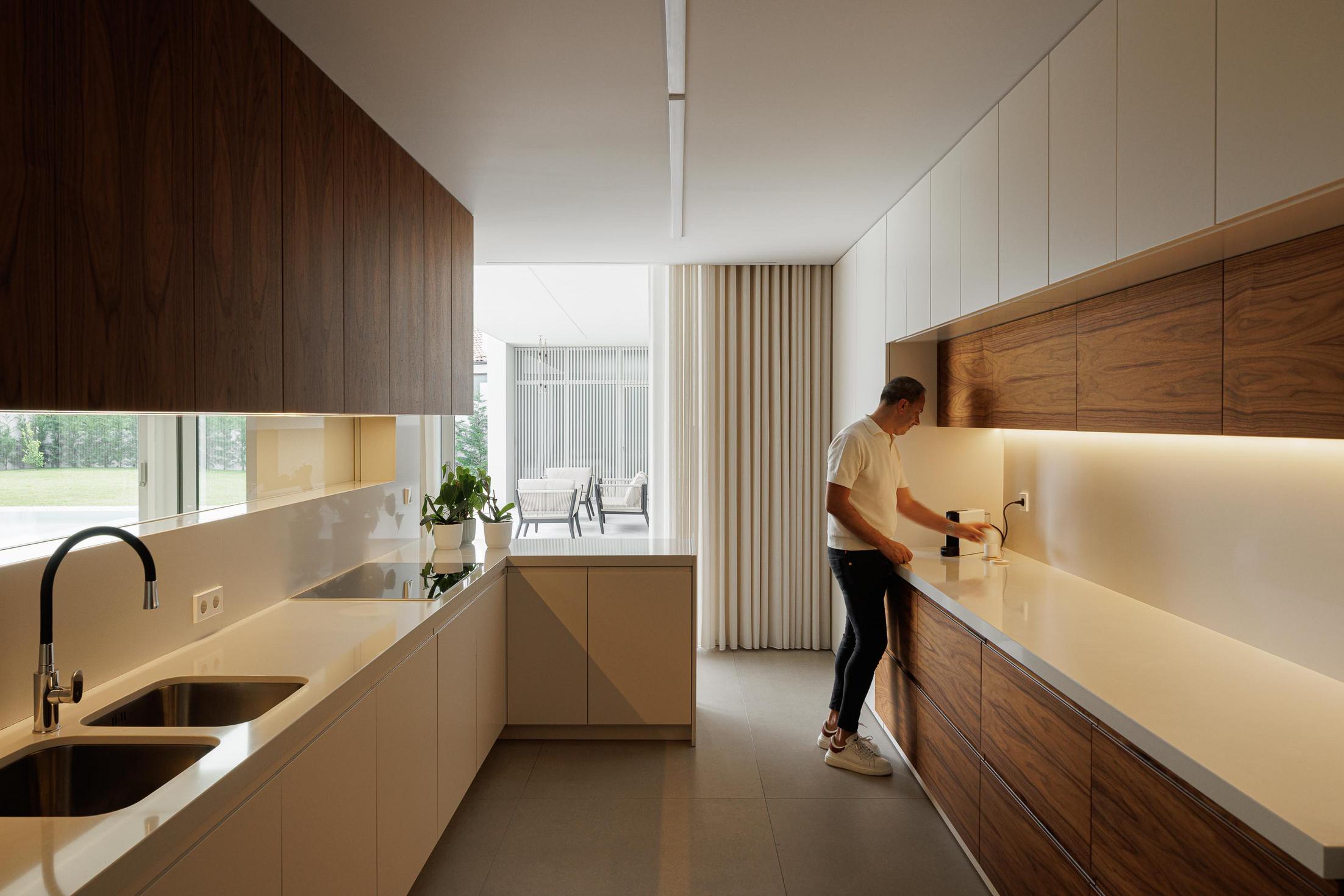 Cozinha: Balcão com cadeiras altas, armários em madeira escura e cortina branca. — Casa Branca Minimalista arquitetura Arquitetura501 em Braga