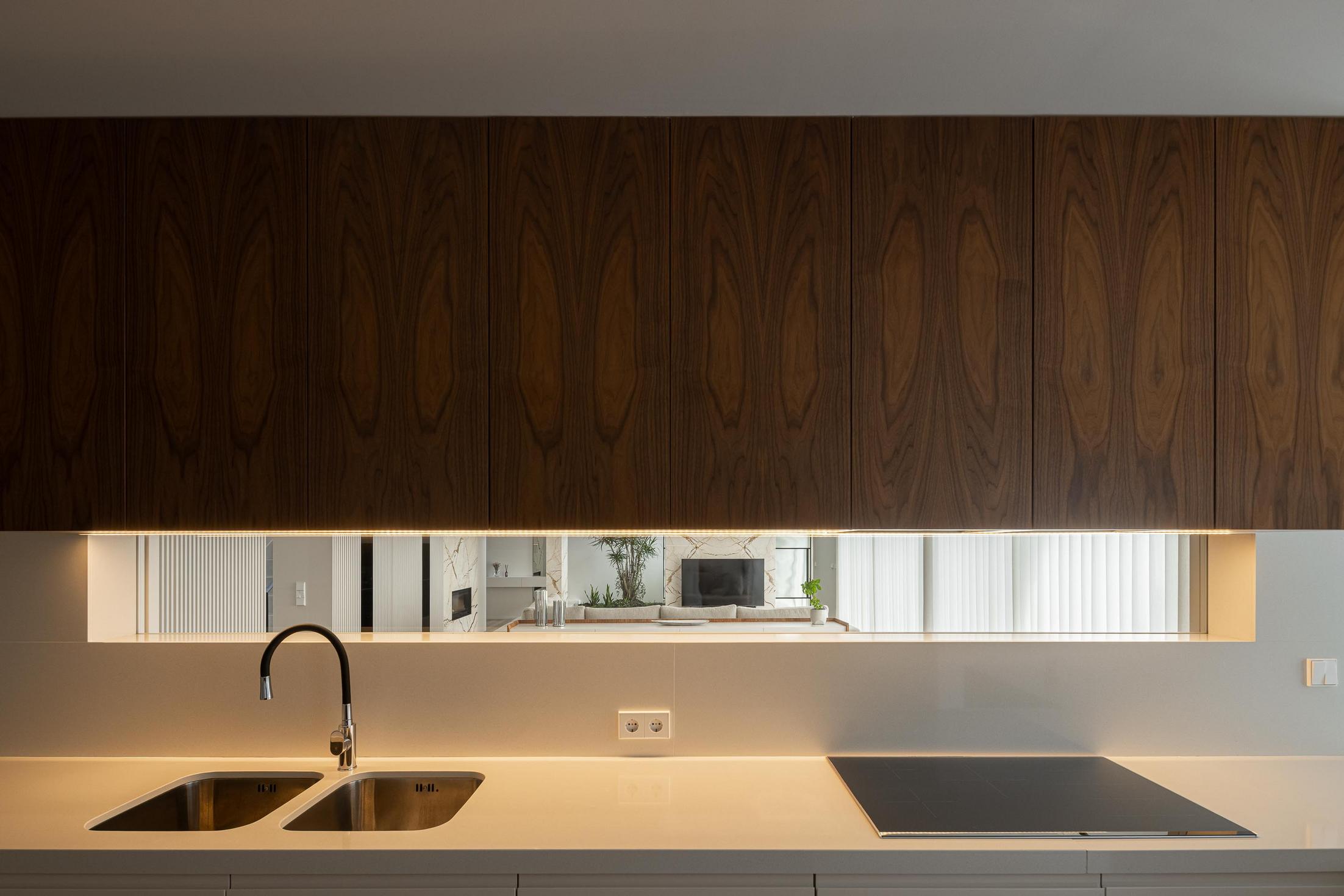 Cozinha: Detalhe da bancada com lavatório, placa de fogão e armários em madeira escura. — Casa Branca Minimalista arquitetura Arquitetura501 em Braga