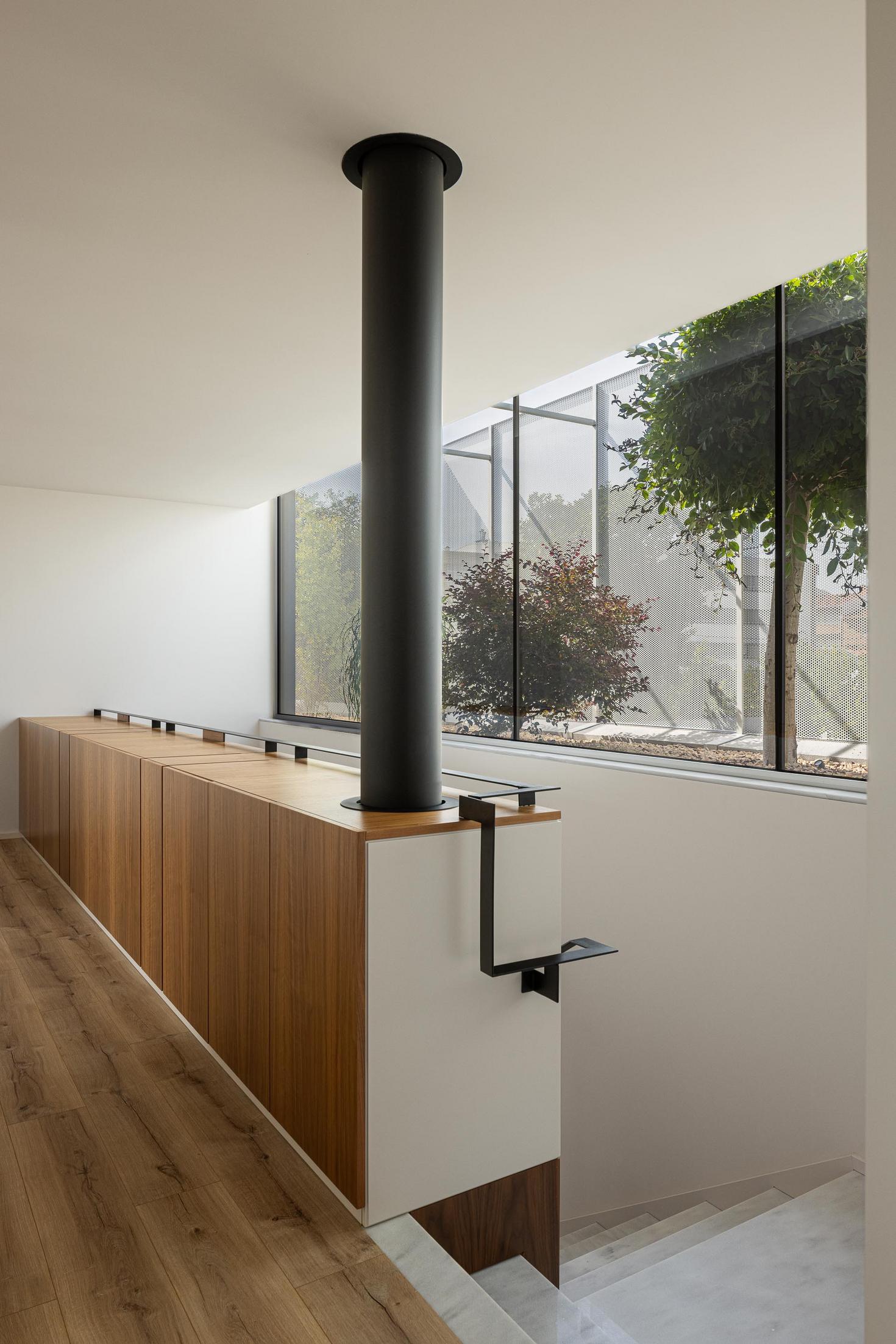 Corredor superior: Guarda-corpo em madeira, escadas em mármore e vista para o jardim interior. — Casa Branca Minimalista arquitetura Arquitetura501 em Braga