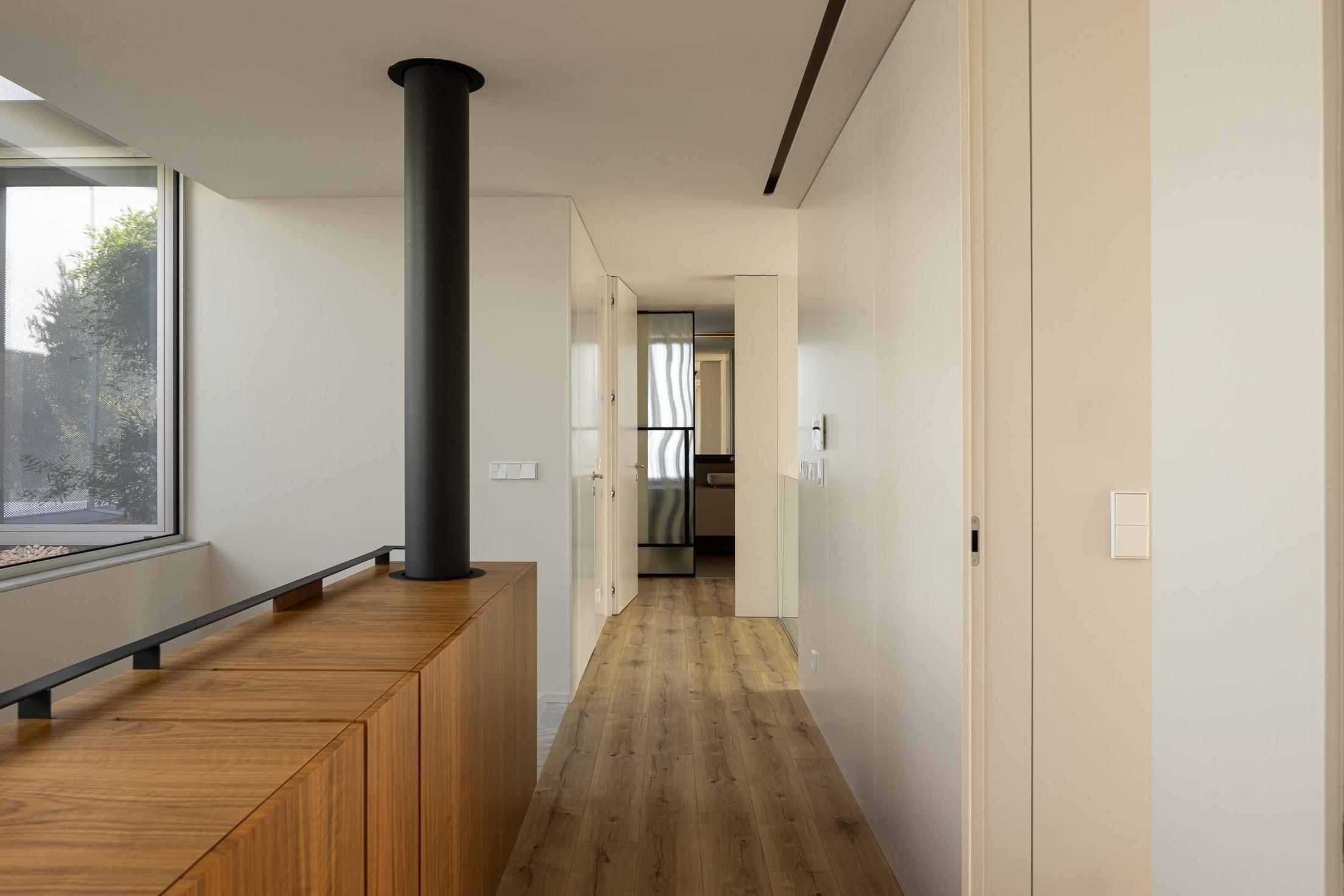 Corredor superior: Vista para o jardim interior e varanda com guarda-corpo em vidro. — Casa Branca Minimalista arquitetura Arquitetura501 em Braga