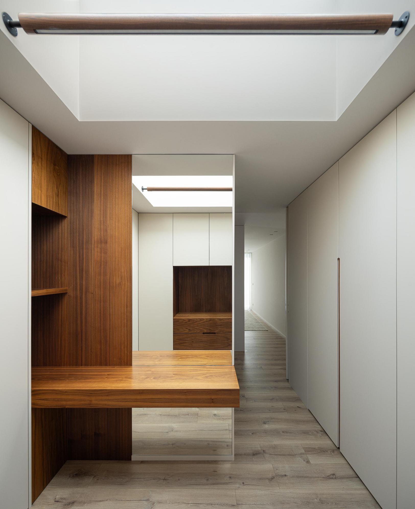 Escritório: Secretária em madeira escura, armários brancos e pavimento em madeira clara sob claraboia. — Casa Branca Minimalista arquitetura Arquitetura501 em Braga