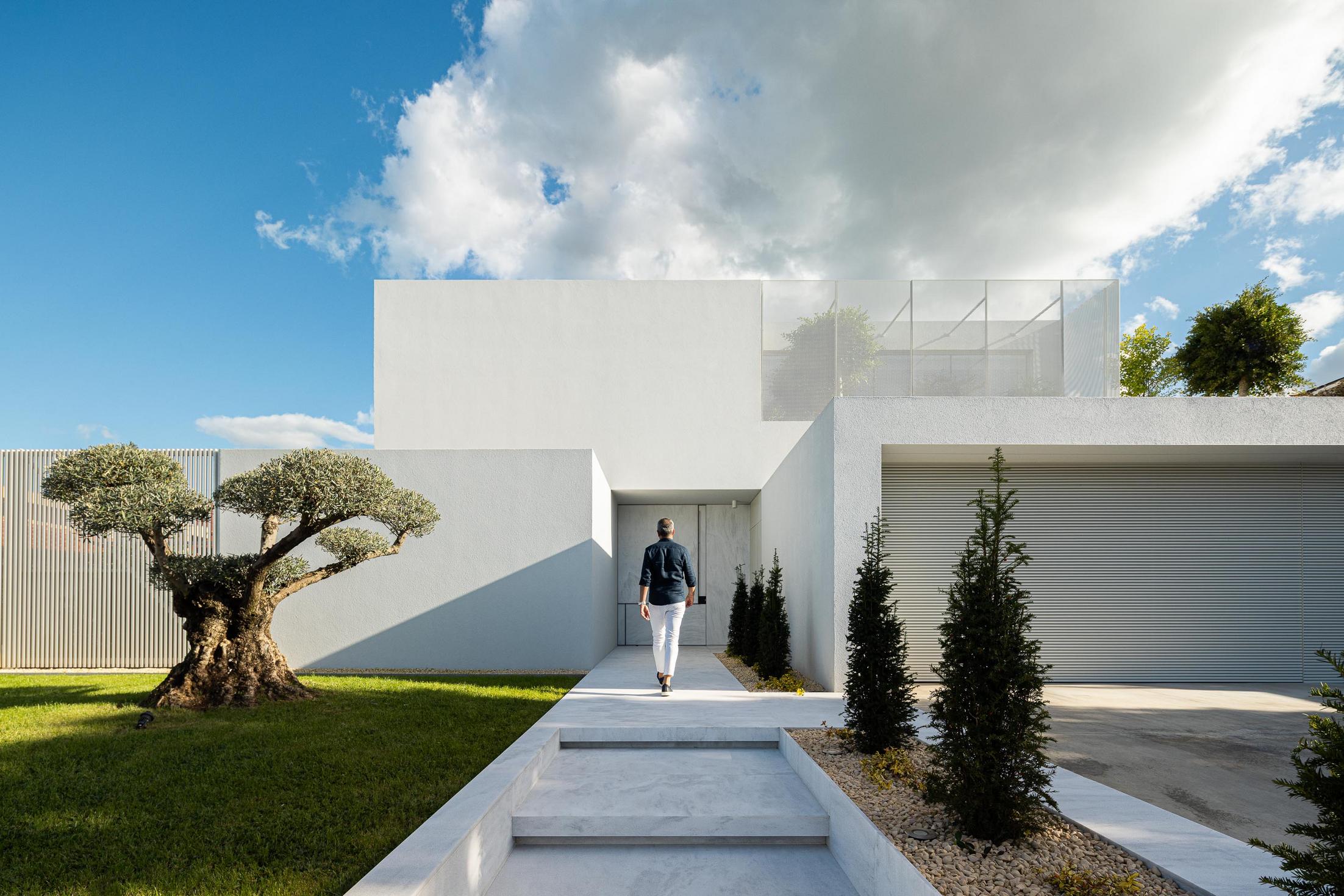Exterior: Fachada frontal da casa com oliveira, escadaria de acesso e garagem. — Casa Branca Minimalista arquitetura Arquitetura501 em Braga