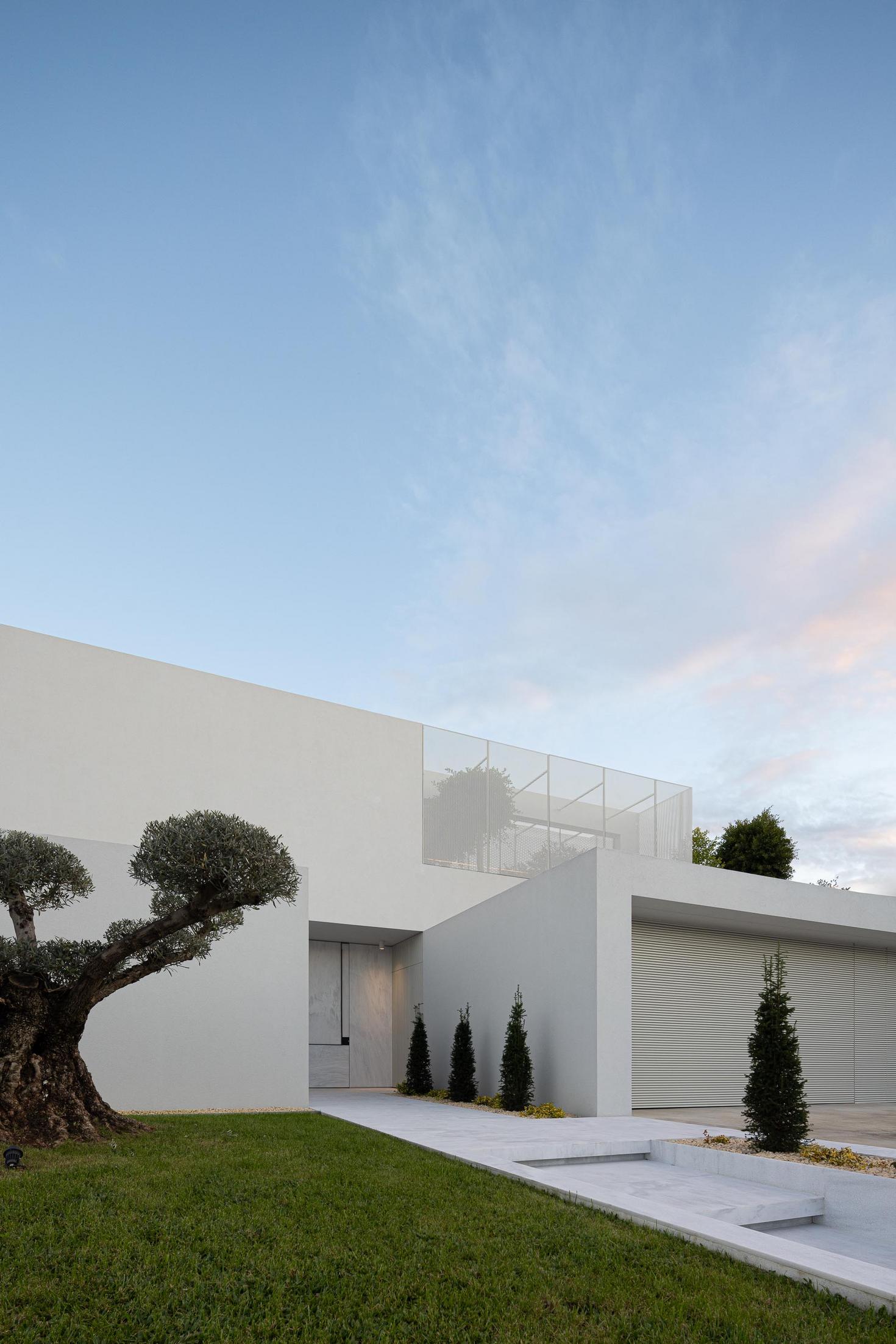 Exterior: Pessoa a olhar para o jardim interior através da janela com revestimento metálico. — Casa Branca Minimalista arquitetura Arquitetura501 em Braga