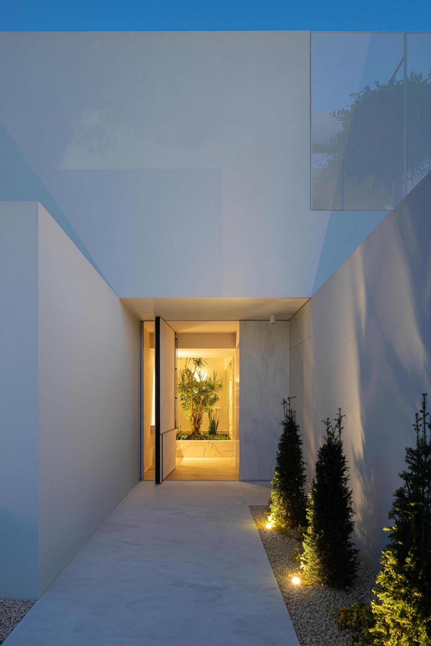 Exterior: Entrada principal da casa, com porta pivotante e jardim interior visível. — Casa Branca Minimalista arquitetura Arquitetura501 em Braga