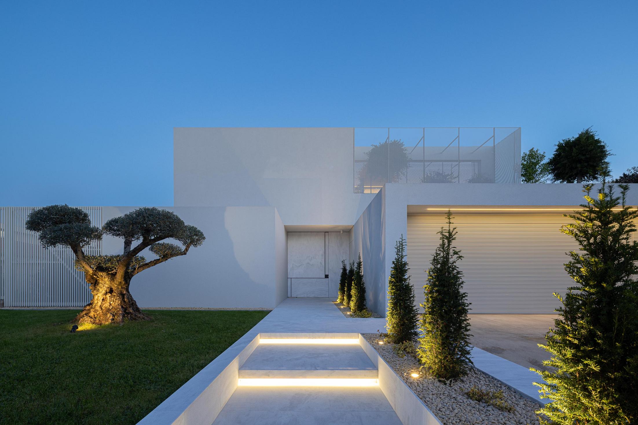 Exterior: Fachada branca minimalista com oliveira e vegetação, sob céu azul. — Casa Branca Minimalista arquitetura Arquitetura501 em Braga
