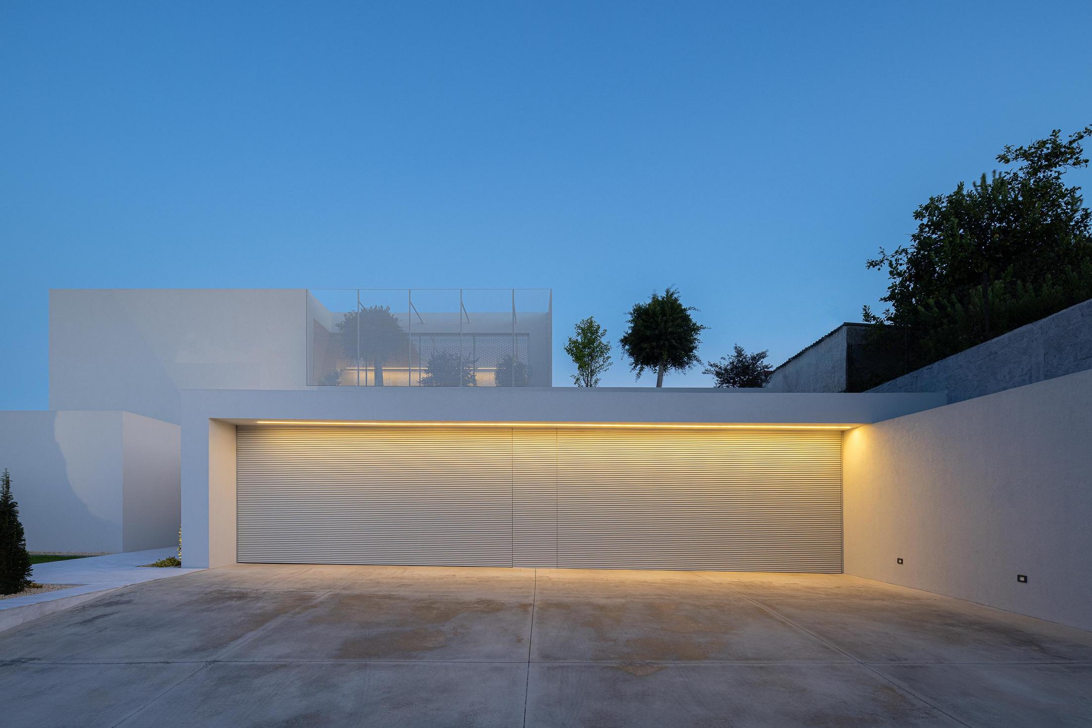 Exterior: Fachada minimalista branca com porta de garagem fechada ao entardecer. — Casa Branca Minimalista arquitetura Arquitetura501 em Braga