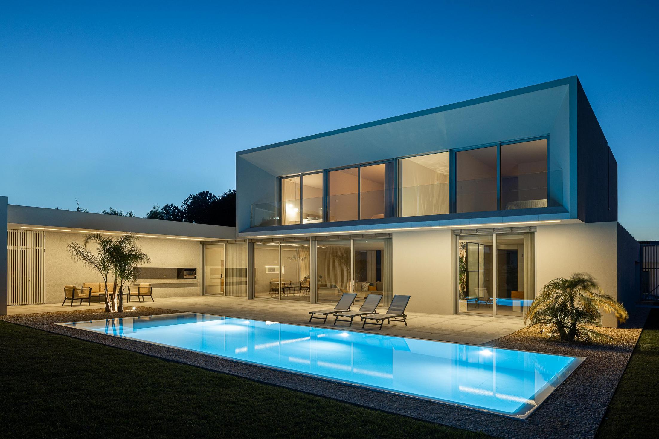 Exterior: Vista geral da casa com piscina, zona de refeições e alpendre ao entardecer. — Casa Branca Minimalista arquitetura Arquitetura501 em Braga