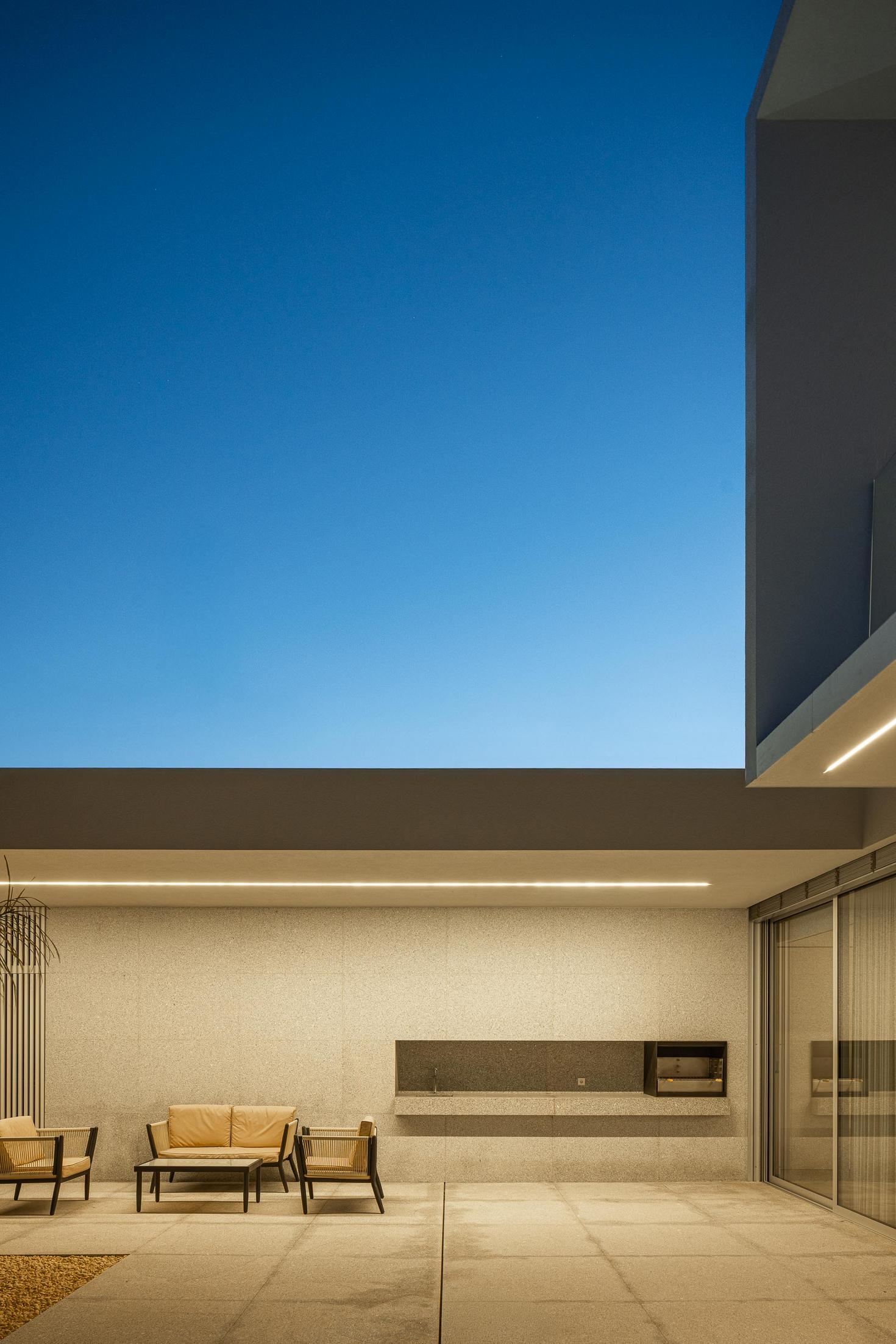 Exterior: Alpendre com zona de estar e churrasqueira, pavimento em pedra e iluminação linear. — Casa Branca Minimalista arquitetura Arquitetura501 em Braga