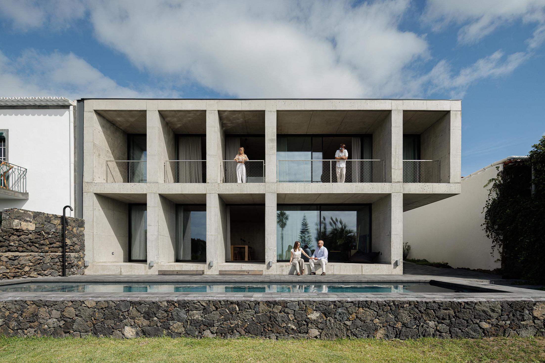 Fachada: Edifício em betão com piscina. Pessoas relaxam nas varandas e junto à piscina. — Casa da Rocha Quebrada arquitetura SO Arquitetura & Design em São Miguel