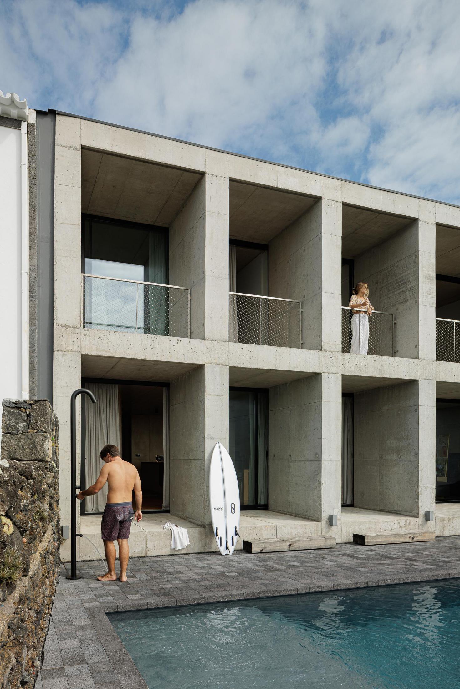 Fachada: Edifício em betão com varandas. Homem a tomar duche junto à piscina. — Casa da Rocha Quebrada arquitetura SO Arquitetura & Design em São Miguel