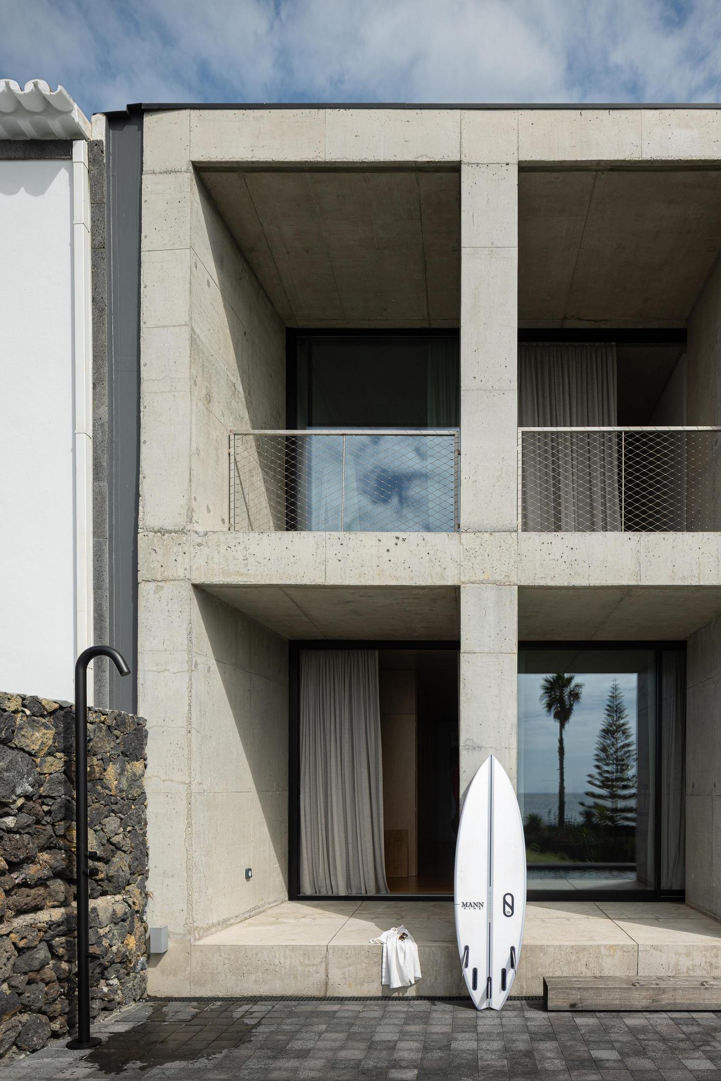 Fachada: Edifício em betão com prancha de surf. Duche exterior e toalha branca. — Casa da Rocha Quebrada arquitetura SO Arquitetura & Design em São Miguel