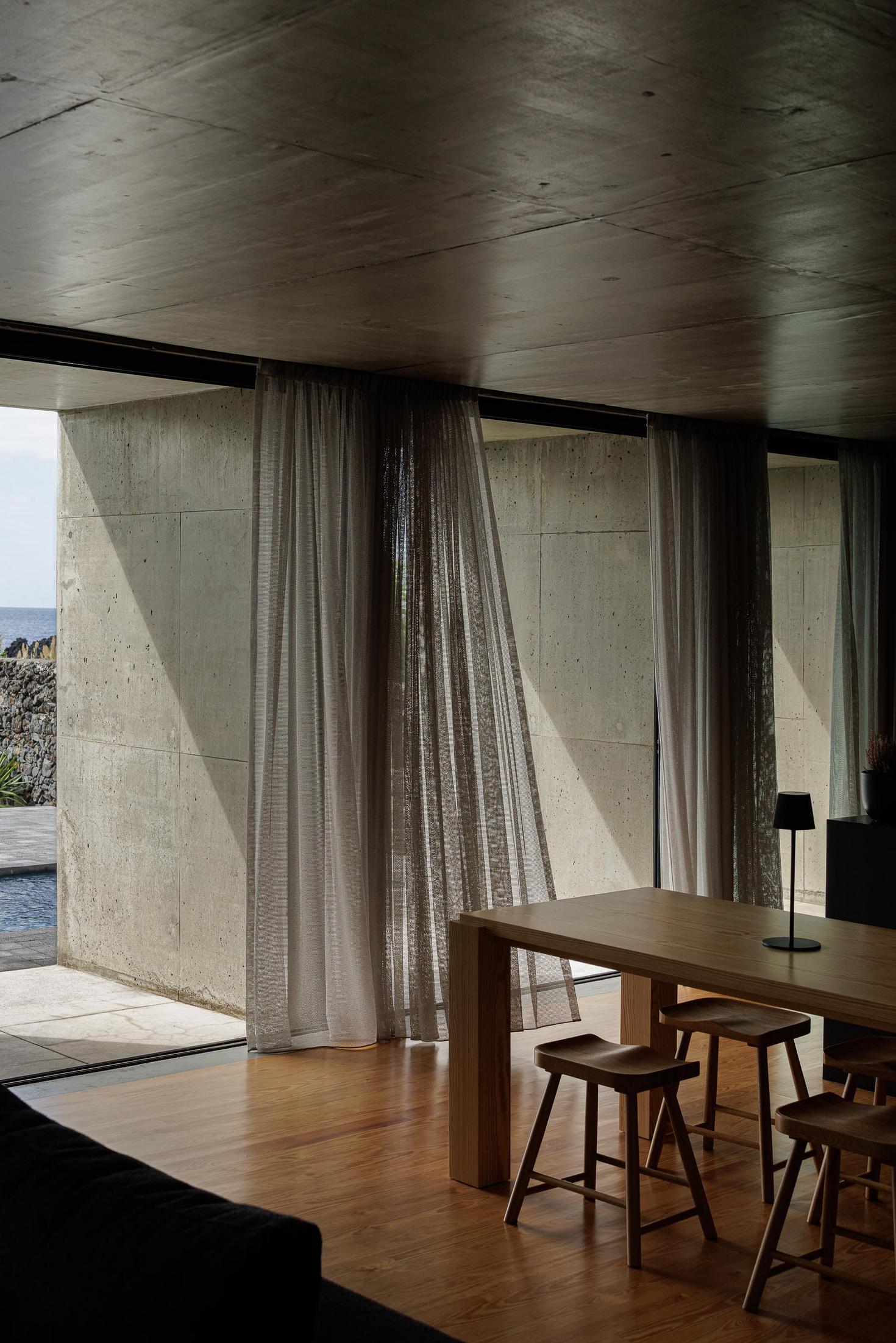Sala de jantar: Mesa de madeira com bancos e cortinas claras. Pavimento em madeira. — Casa da Rocha Quebrada arquitetura SO Arquitetura & Design em São Miguel