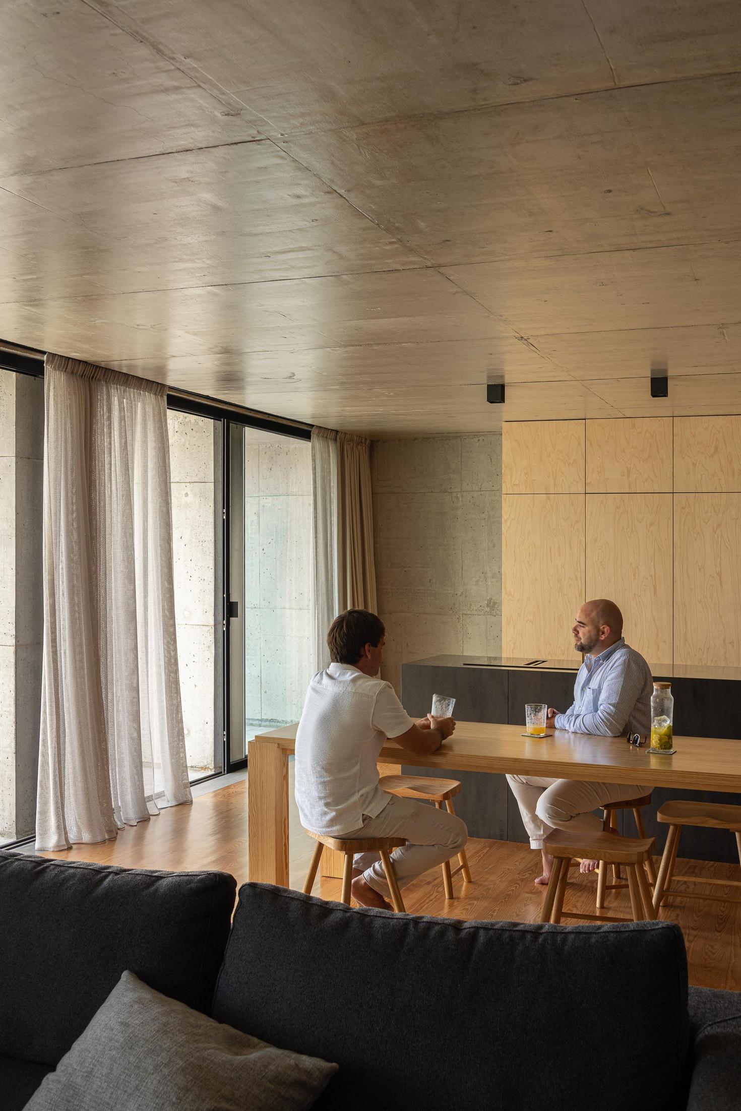 Sala de estar: Pessoas sentadas à mesa em madeira. Sofá cinzento e cortinas claras. — Casa da Rocha Quebrada arquitetura SO Arquitetura & Design em São Miguel