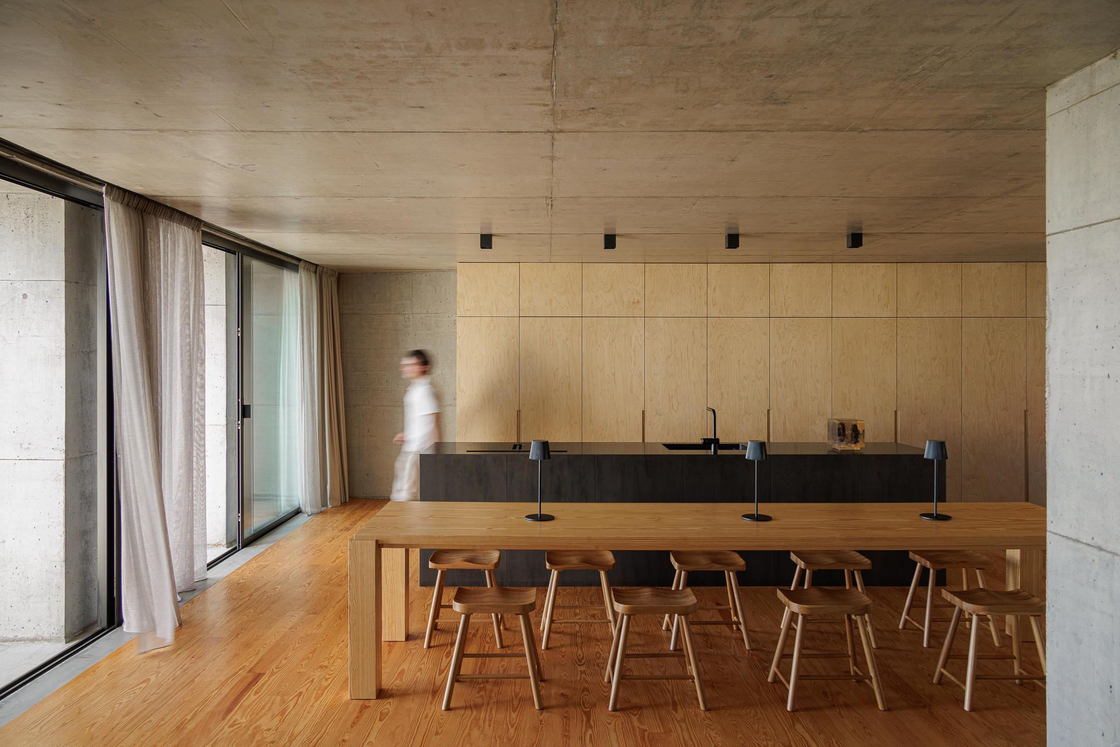 Cozinha: Mesa de jantar em madeira com bancos. Armários em contraplacado e parede em betão. — Casa da Rocha Quebrada arquitetura SO Arquitetura & Design em São Miguel