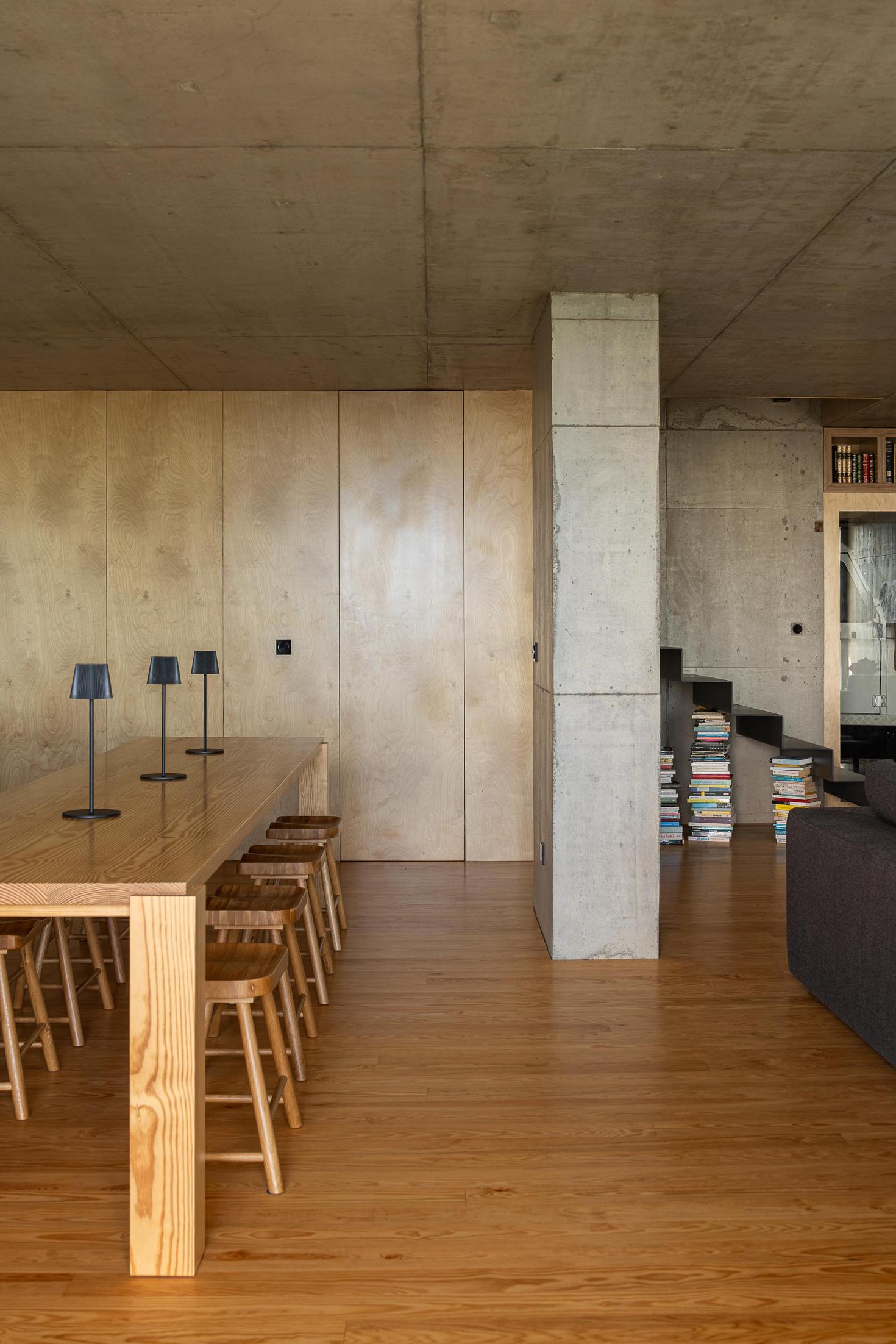 Sala de jantar: Mesa comprida em madeira com bancos. Pavimento em madeira e parede em betão. — Casa da Rocha Quebrada arquitetura SO Arquitetura & Design em São Miguel
