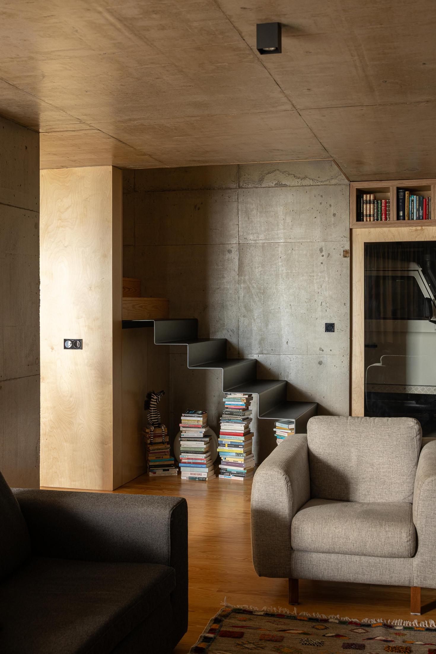 Sala de estar: Escadas pretas e cadeirões cinzentos. Pavimento em madeira e parede em betão. — Casa da Rocha Quebrada arquitetura SO Arquitetura & Design em São Miguel